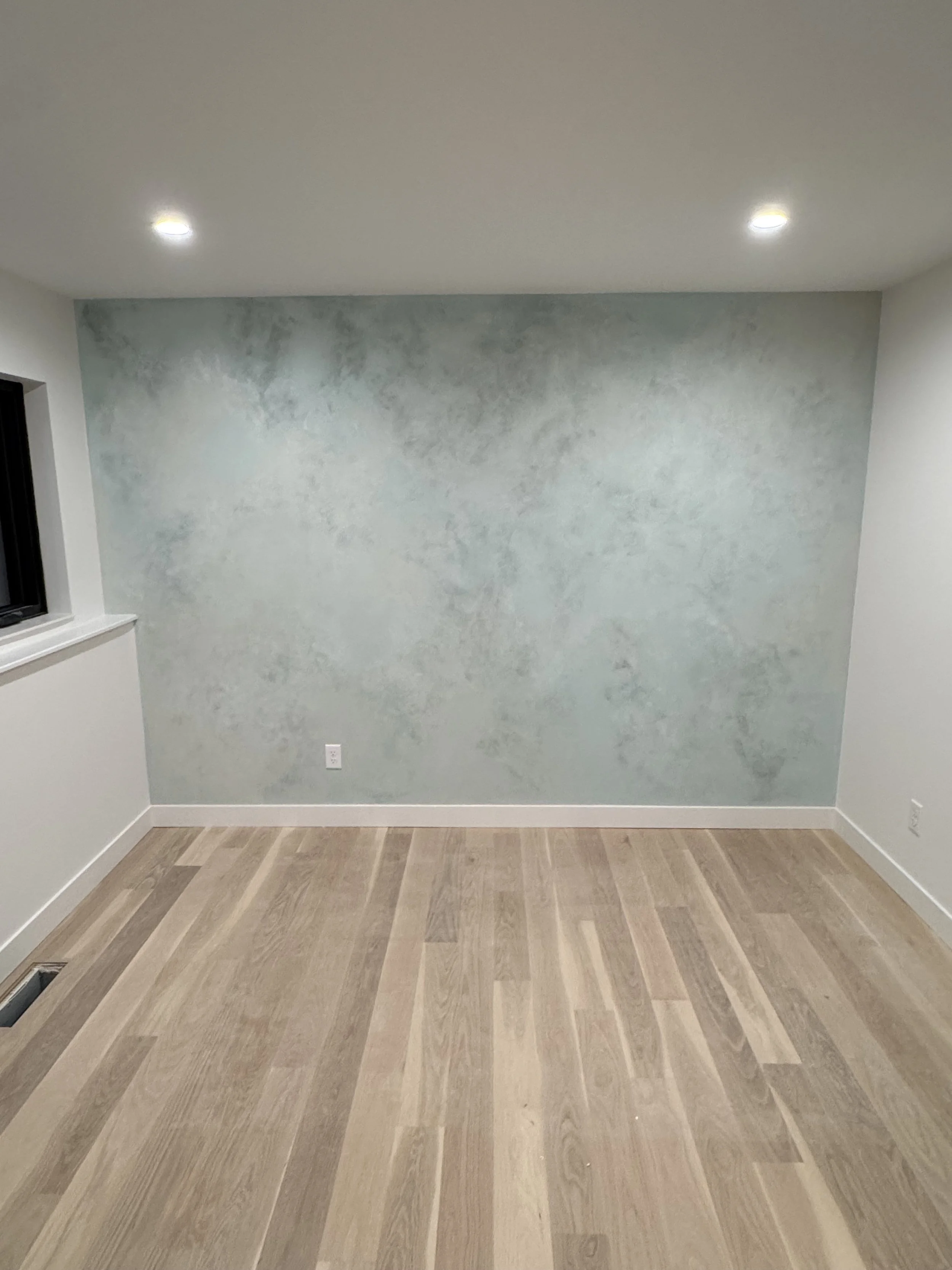Empty room with a light blue textured wall, wood flooring, and recessed ceiling lights.