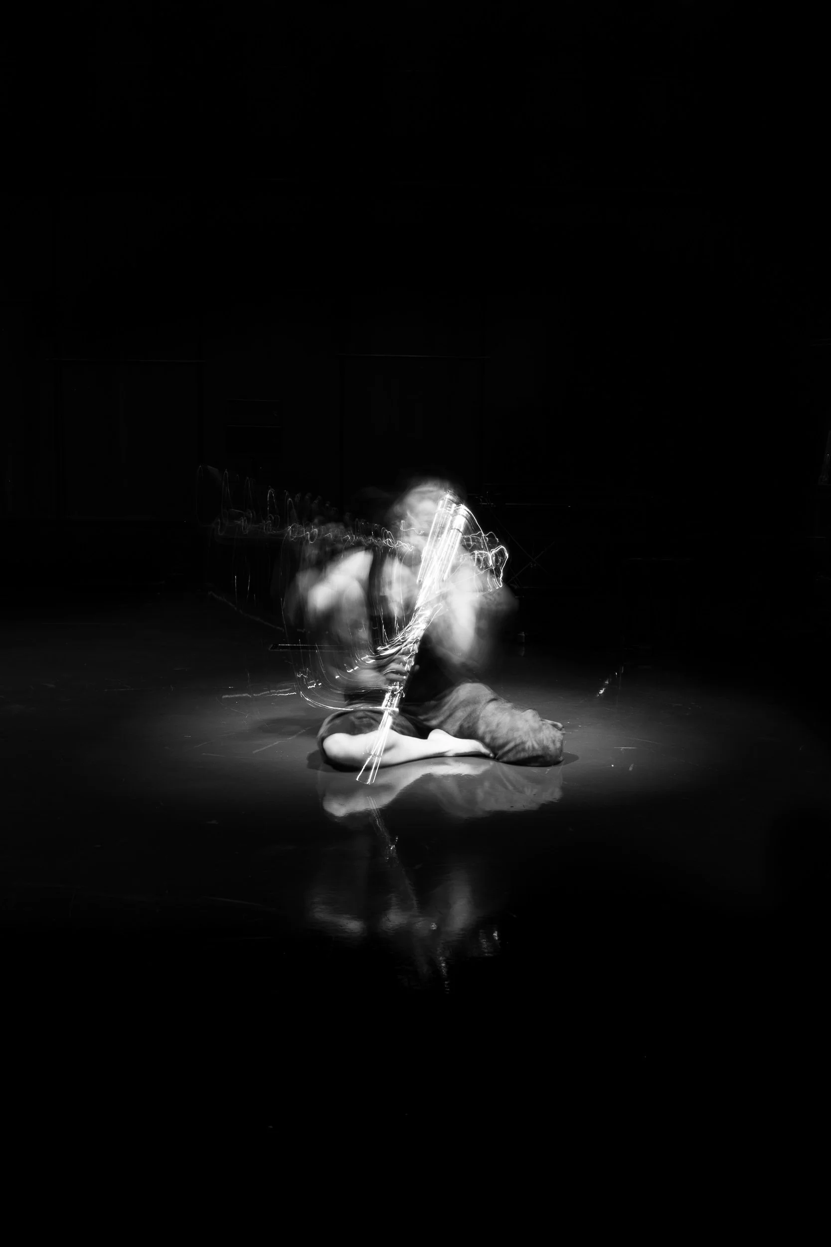 A person sitting on the floor playing a saxophone, with motion blur and light trails affecting the image, in a dark environment.