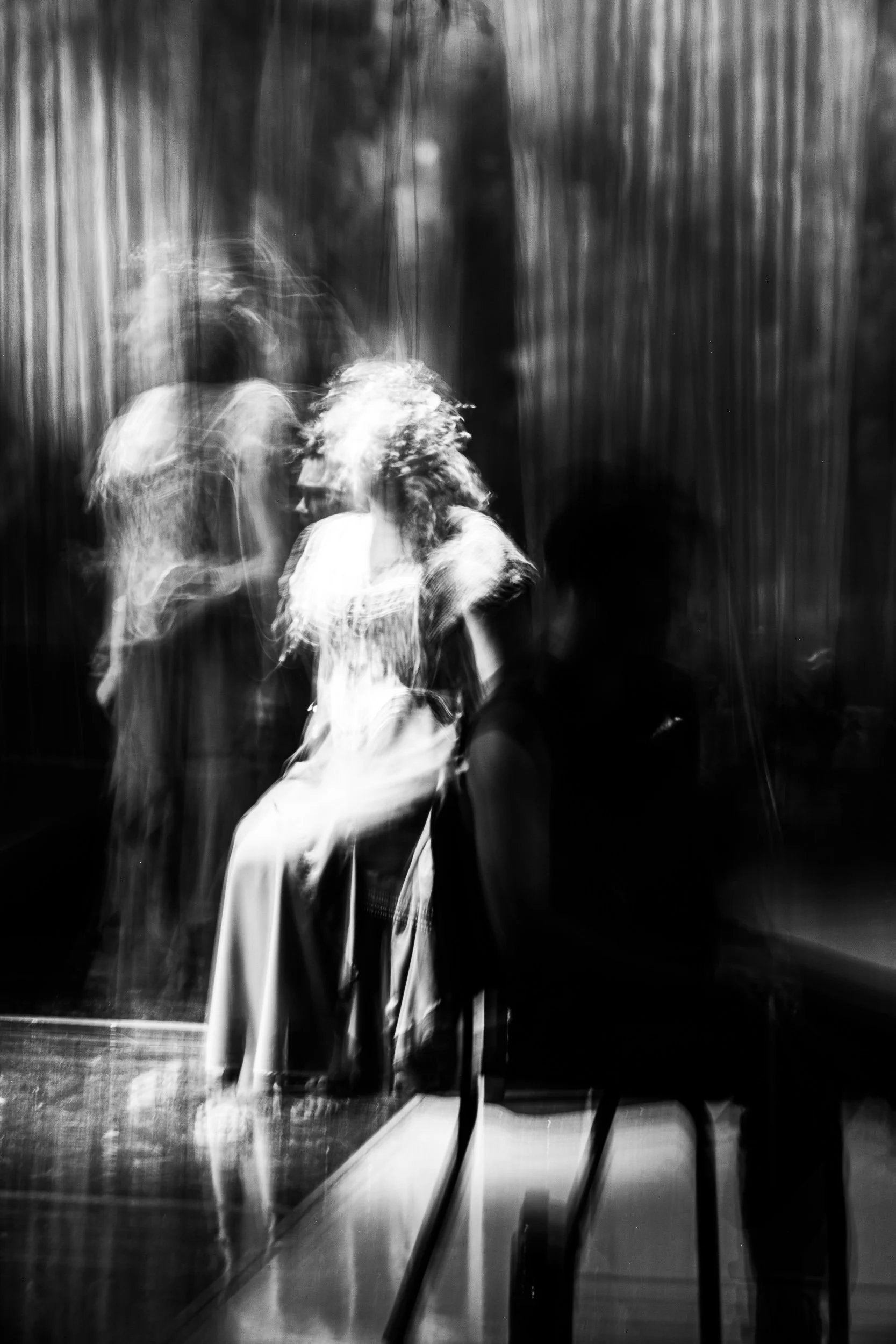 Black and white photograph of two women sitting in a dimly lit room with blurred motion effects, creating ghostly figures.