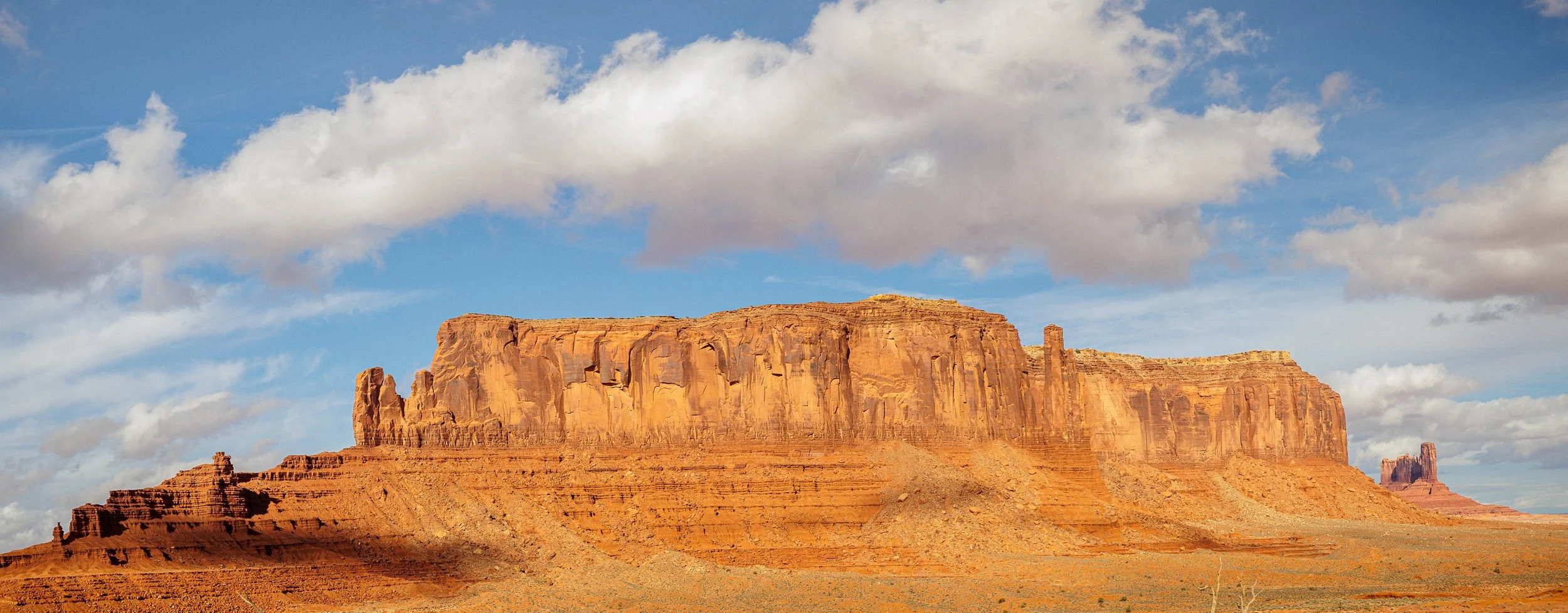 View of a large butte formation in a desert landscape with partly cloudy sky.
