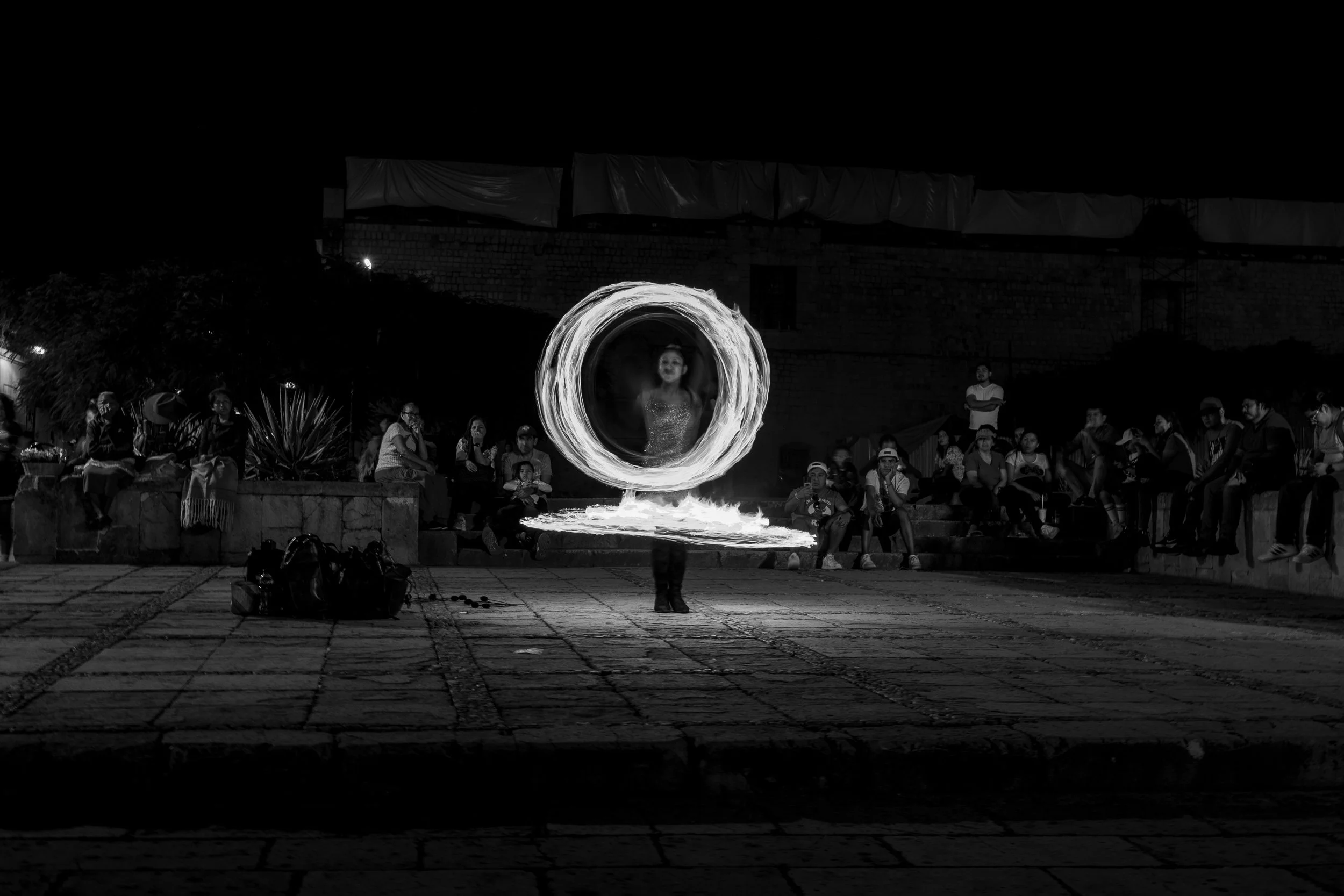 A performer creating a fire spinning circle in front of an audience on a dark night.