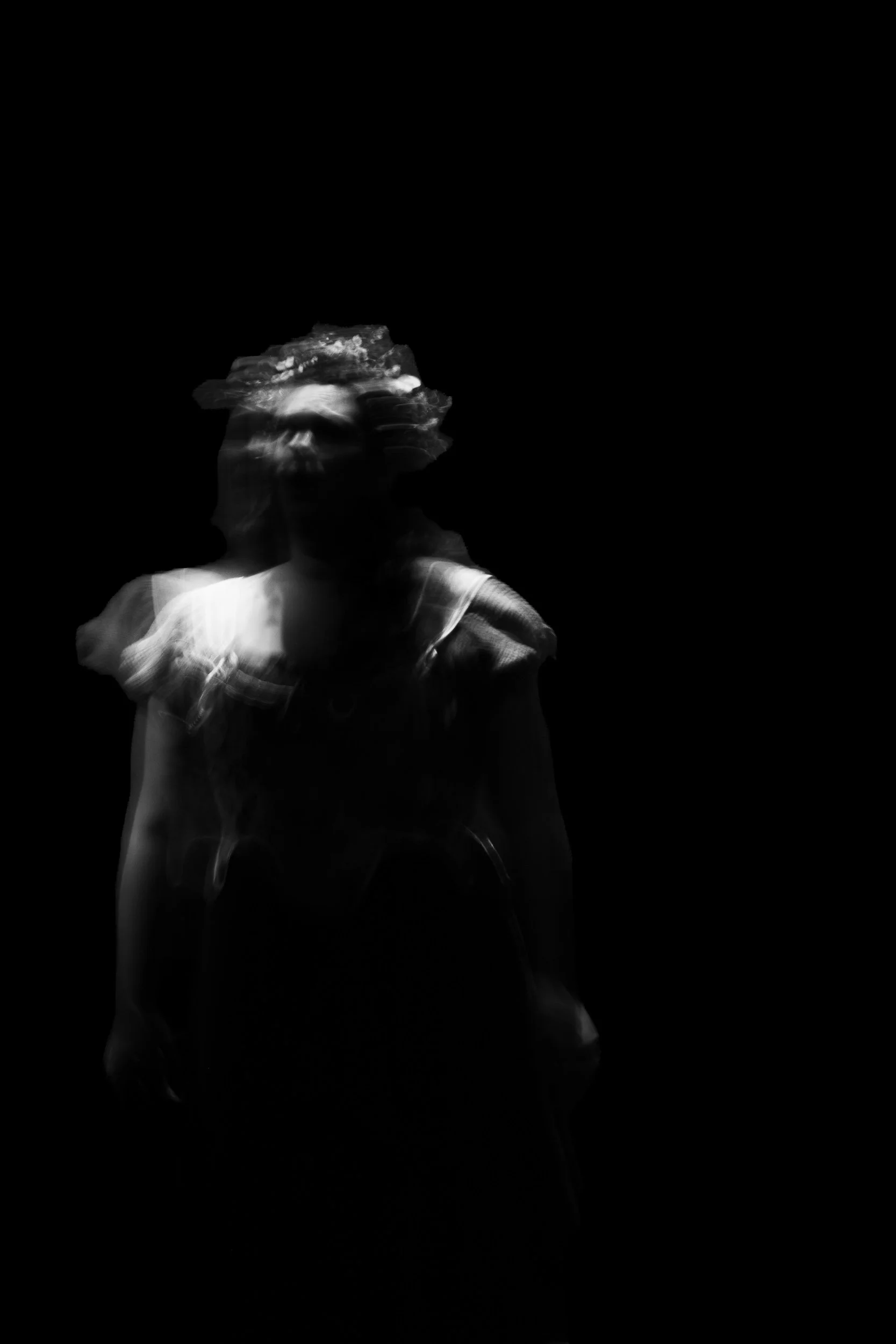 A blurred black-and-white photo of a young girl with curly hair, wearing a dress with ruffled sleeves, standing in darkness.