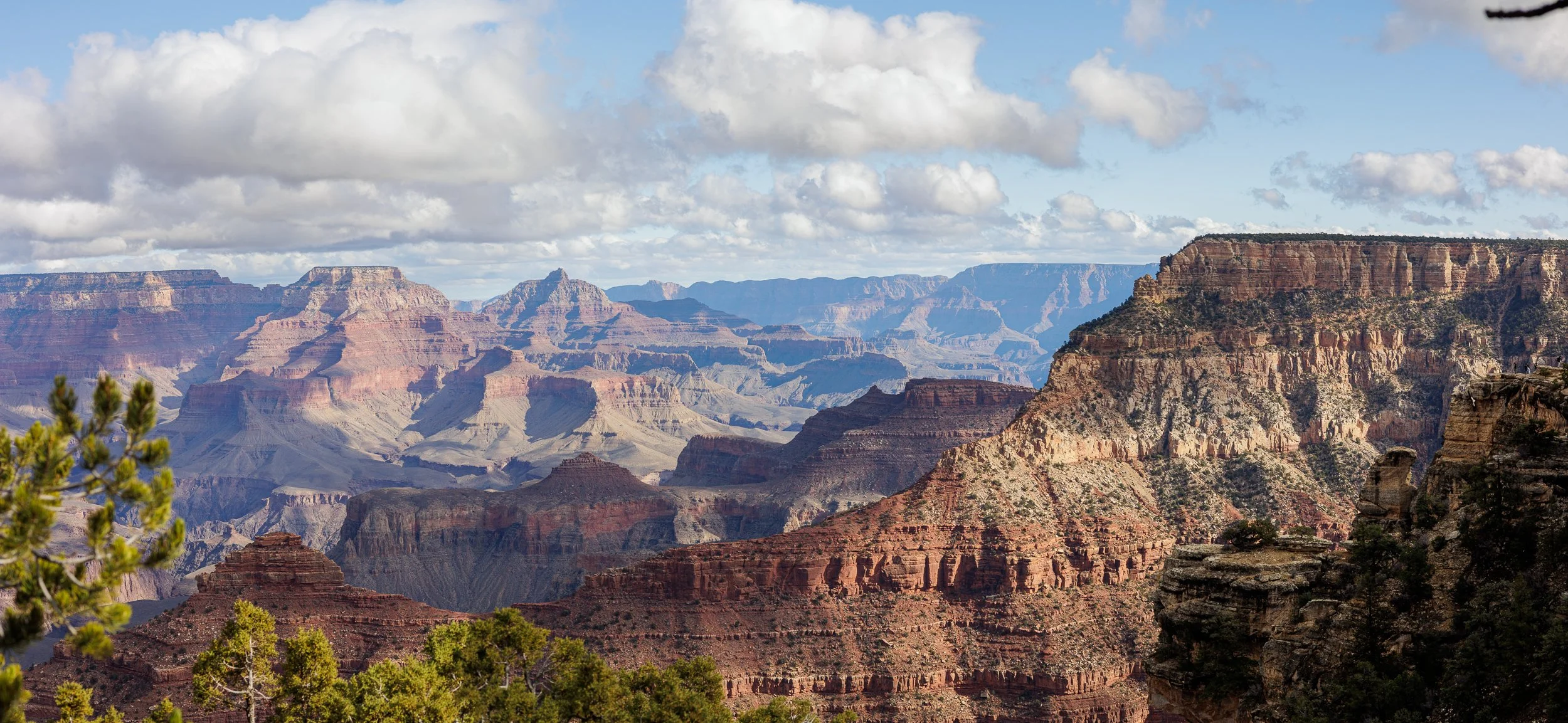 Panoramic view of the Grand Canyon showcasing layered rock formations and cliffs under a sky with scattered clouds.