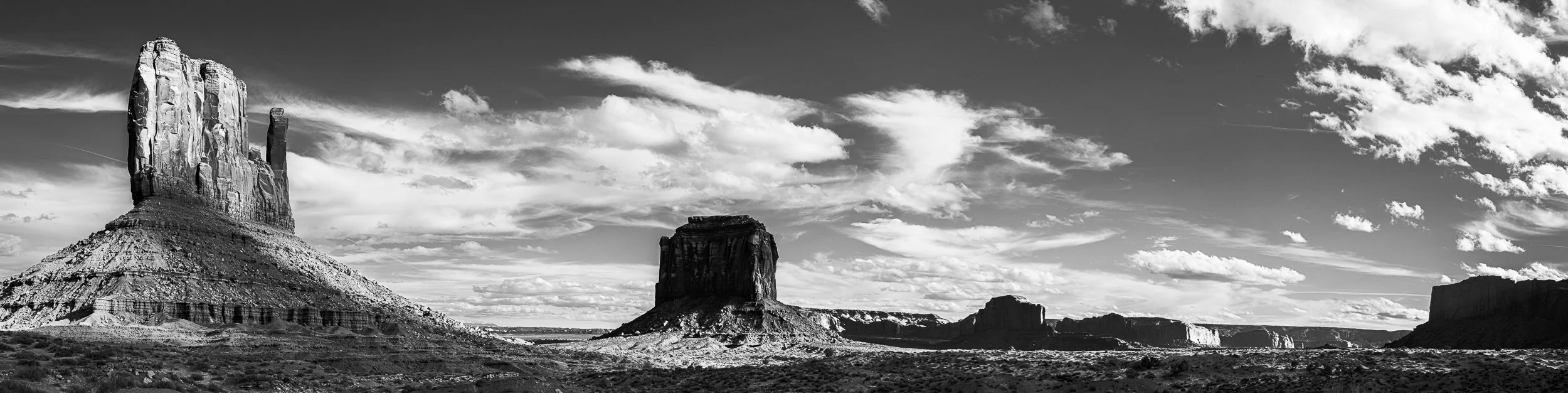 Black and white photo of a desert landscape with large buttes and mesas under a cloudy sky.