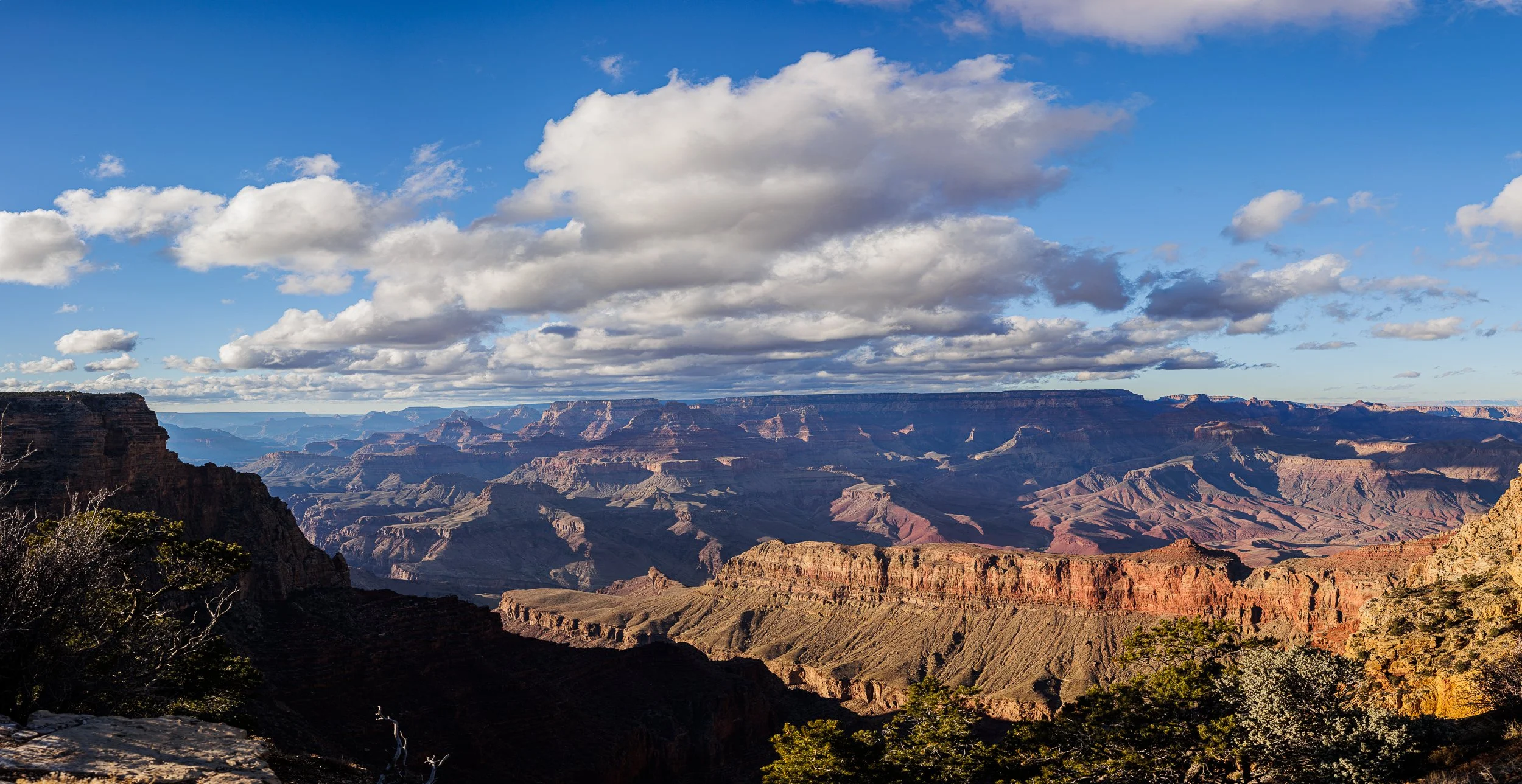 A view of the Grand Canyon with layered red and brown rock formations under a blue sky with white clouds.