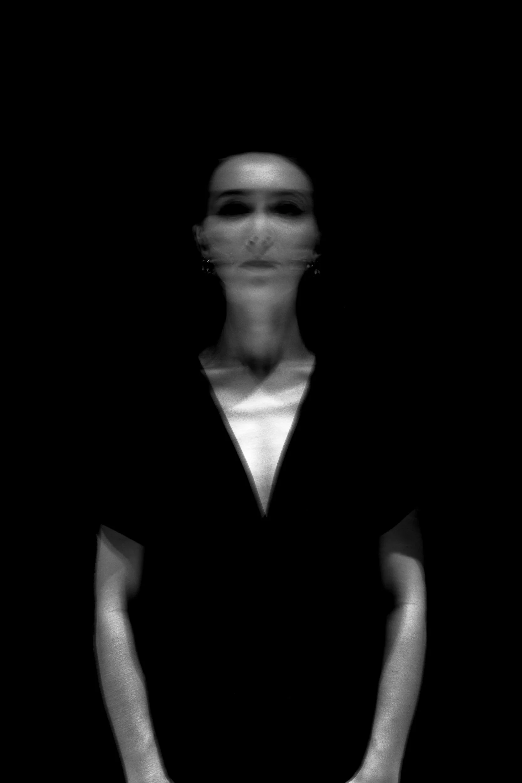 Blurry black-and-white portrait of a woman with dark hair, wearing earrings, against a dark background.