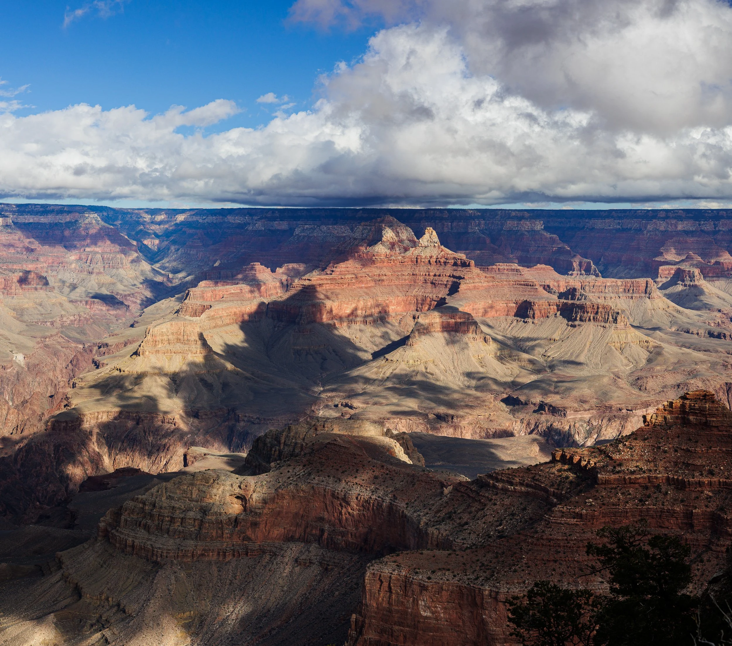 Photo of the Grand Canyon with layered red and brown rocks, shadowed areas, and a partly cloudy sky.