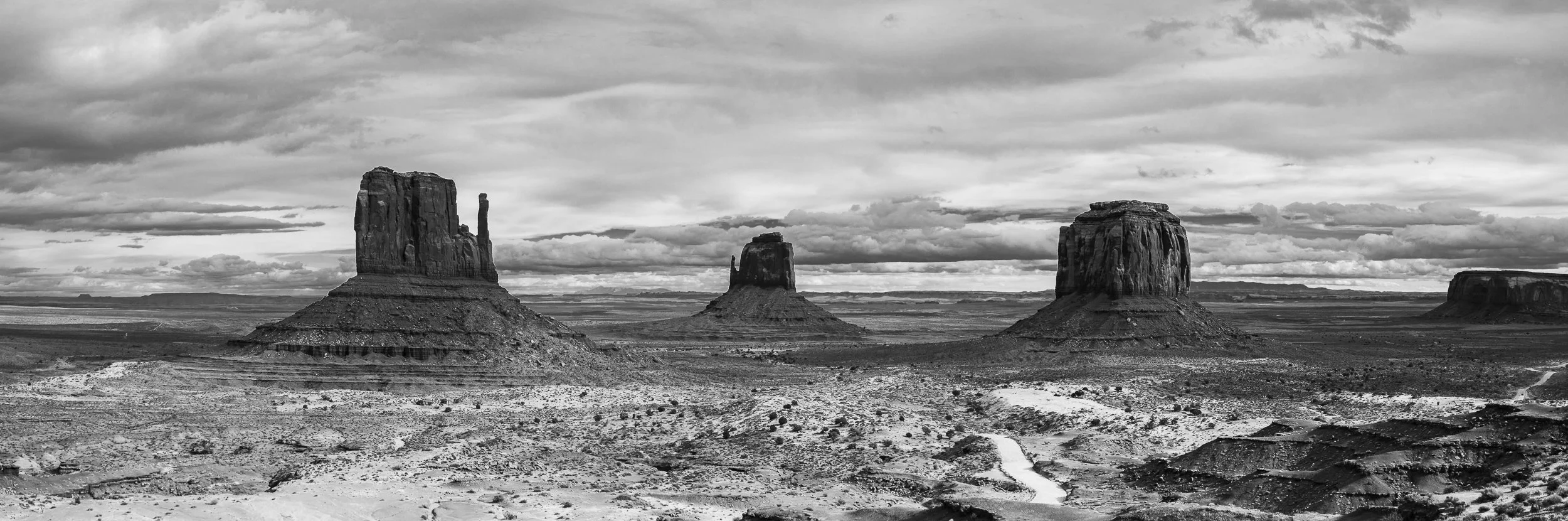 Black and white photograph of the desert landscape featuring three large, isolated rock formations under a cloudy sky.