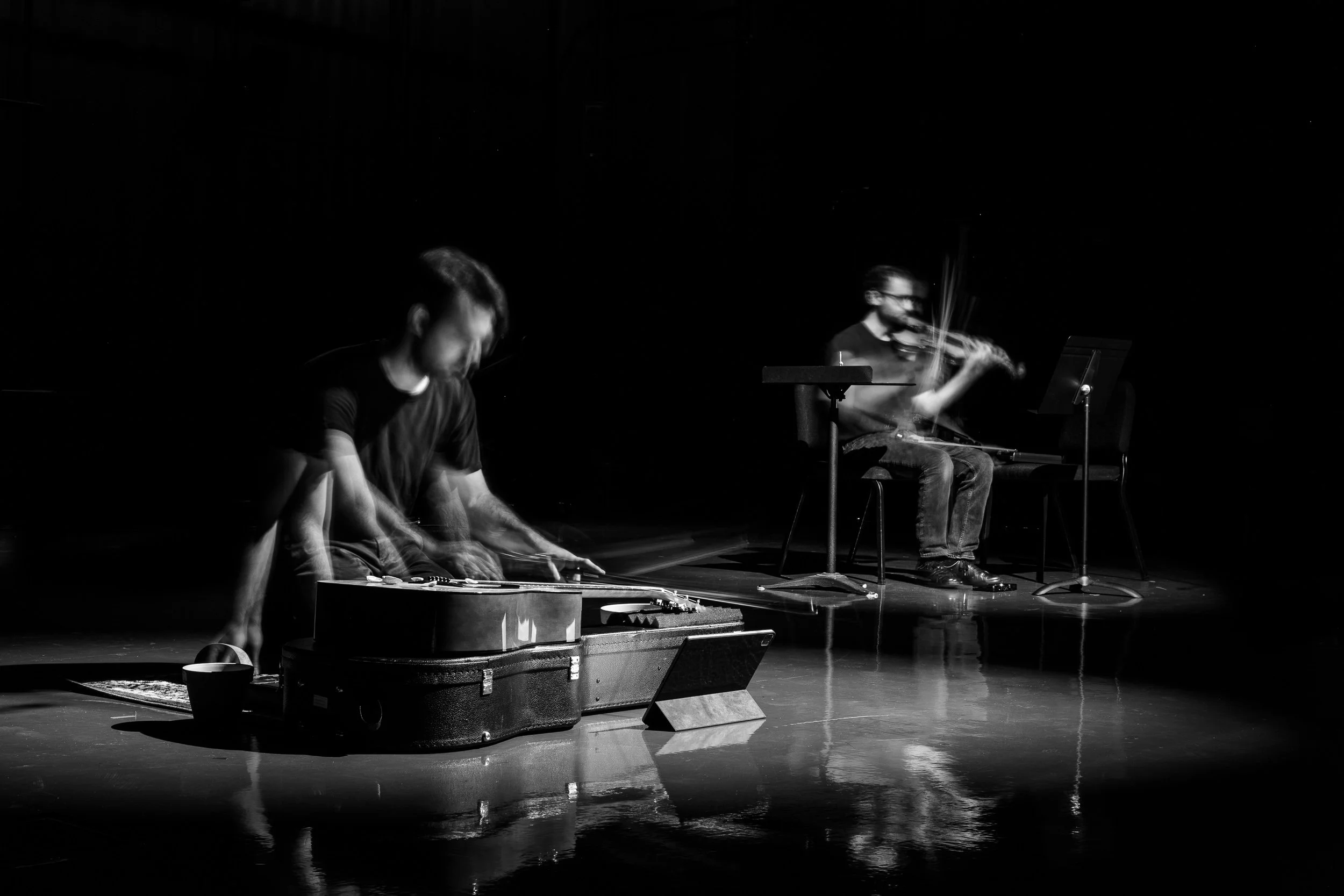 Two musicians performing on a dark stage, one playing a keyboard and the other playing a violin, with motion blur indicating movement.