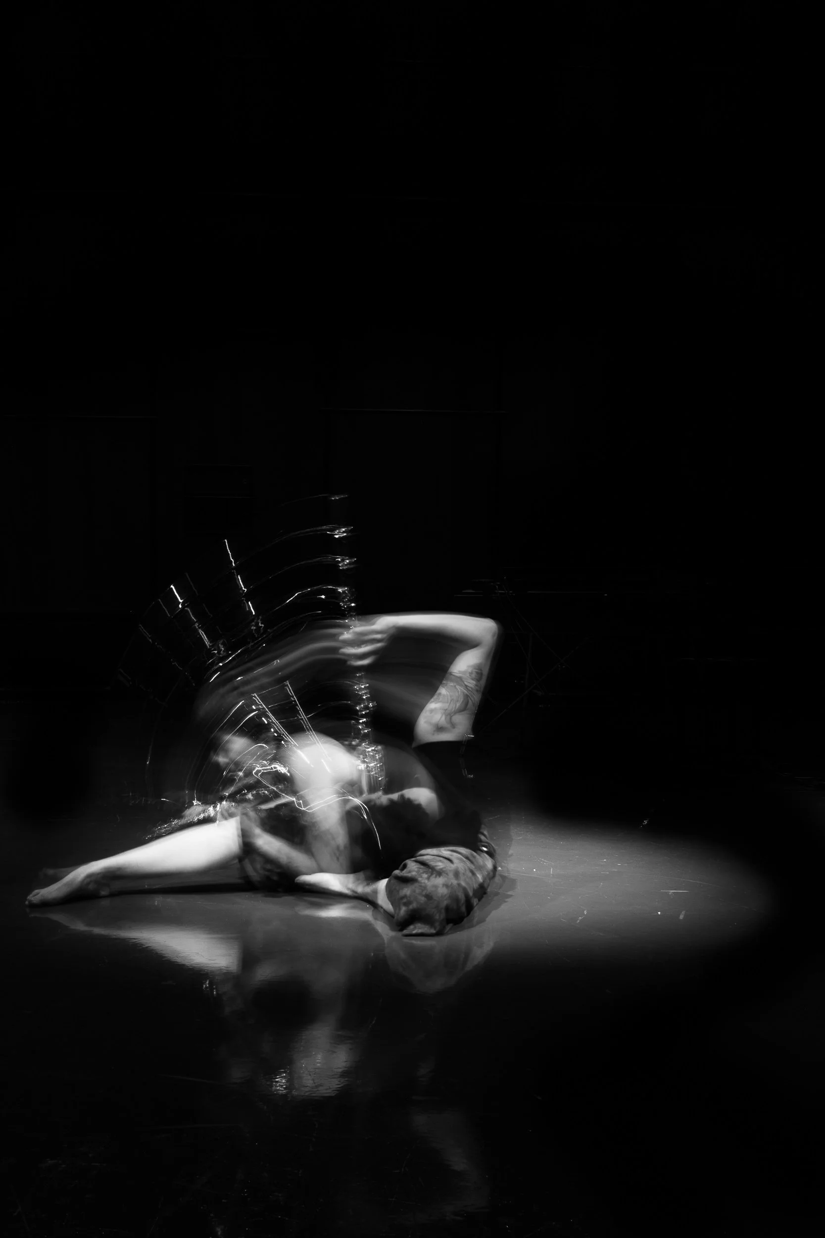 Black and white photo of a person lying on the floor in a pose, with motion blur around them indicating movement.