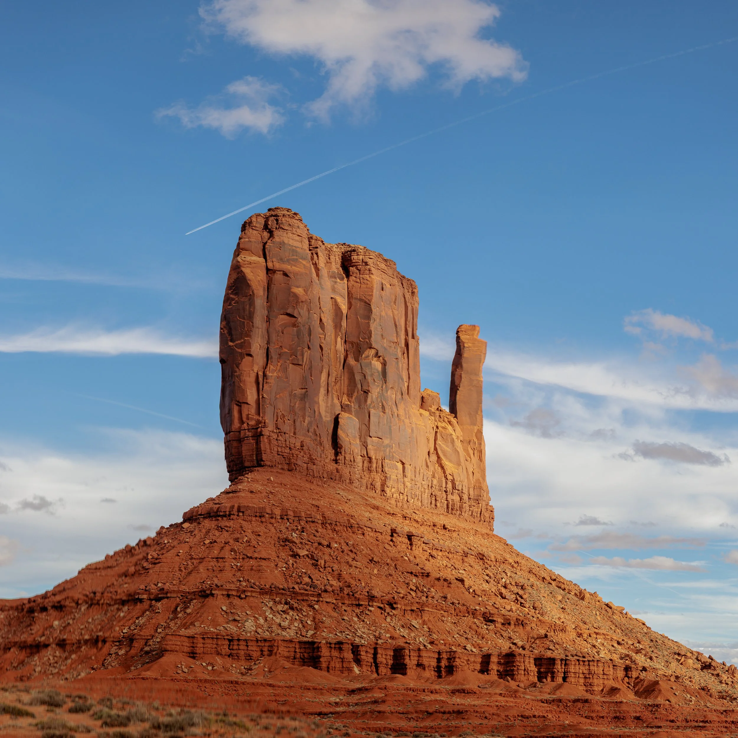 Red rock formation in desert landscape with blue sky and scattered clouds.
