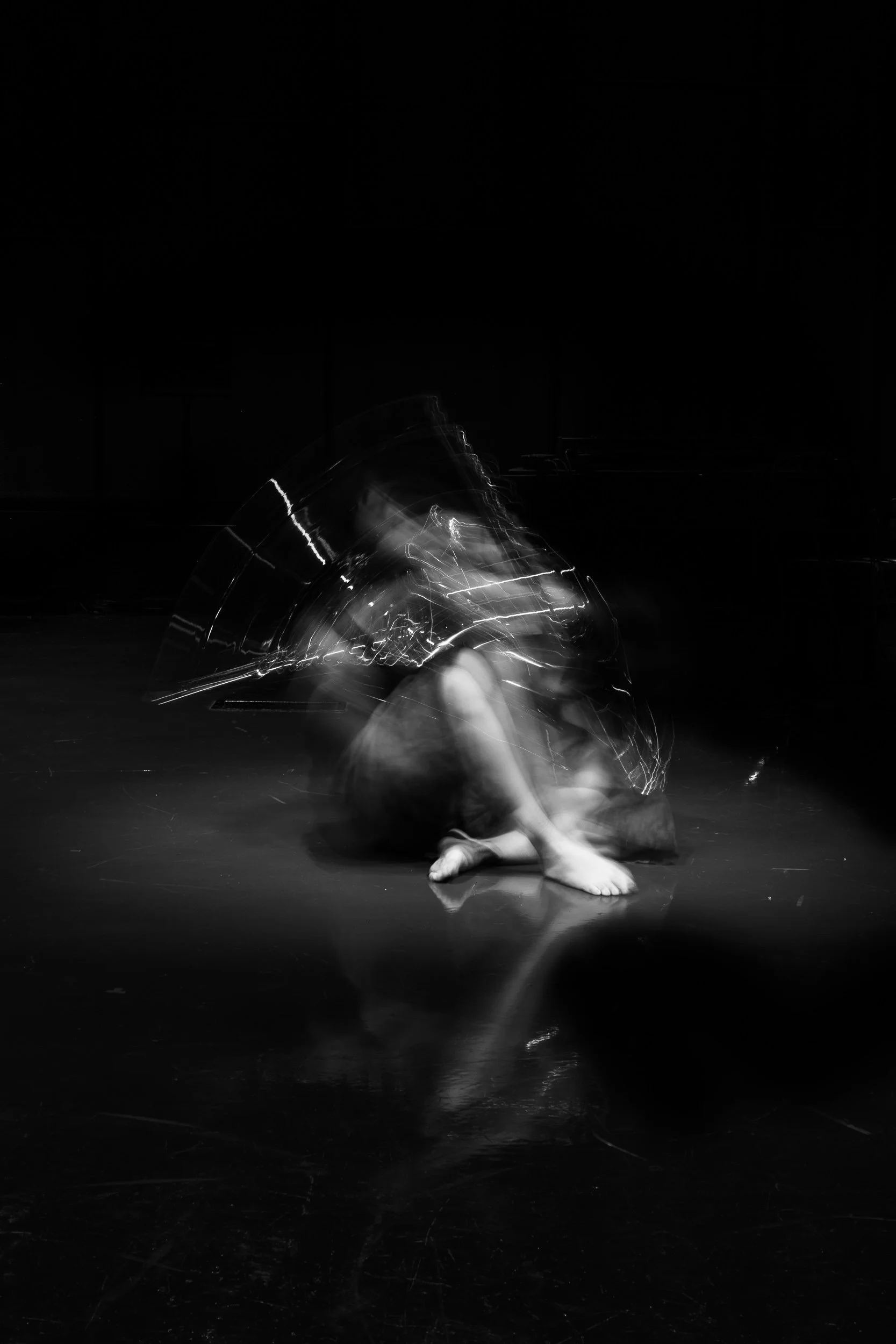 Black and white photo of a dancer in motion, with a blurred, glowing umbrella and a dark background.