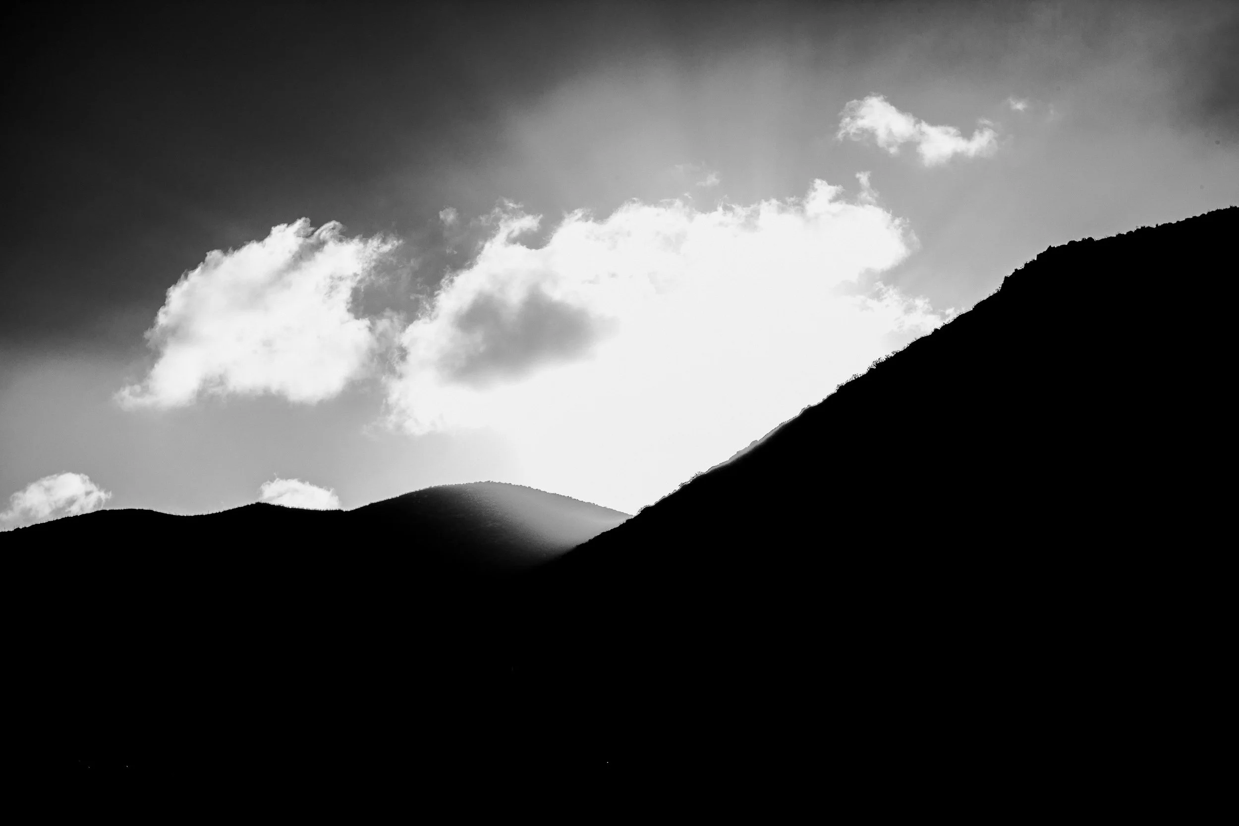 Black and white photograph of mountain ridges with clouds in the sky.