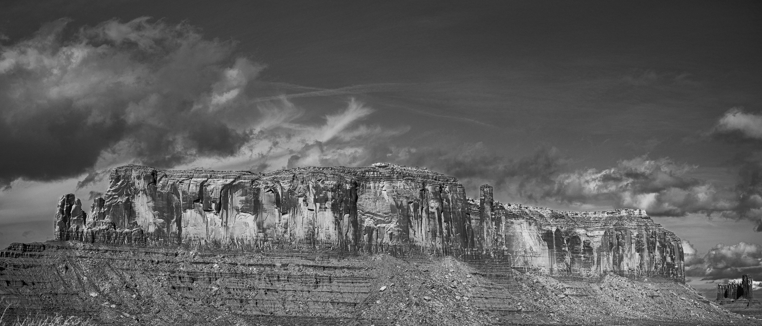 Black and white photograph of a large mountain with steep, layered cliffs, under a cloudy sky.