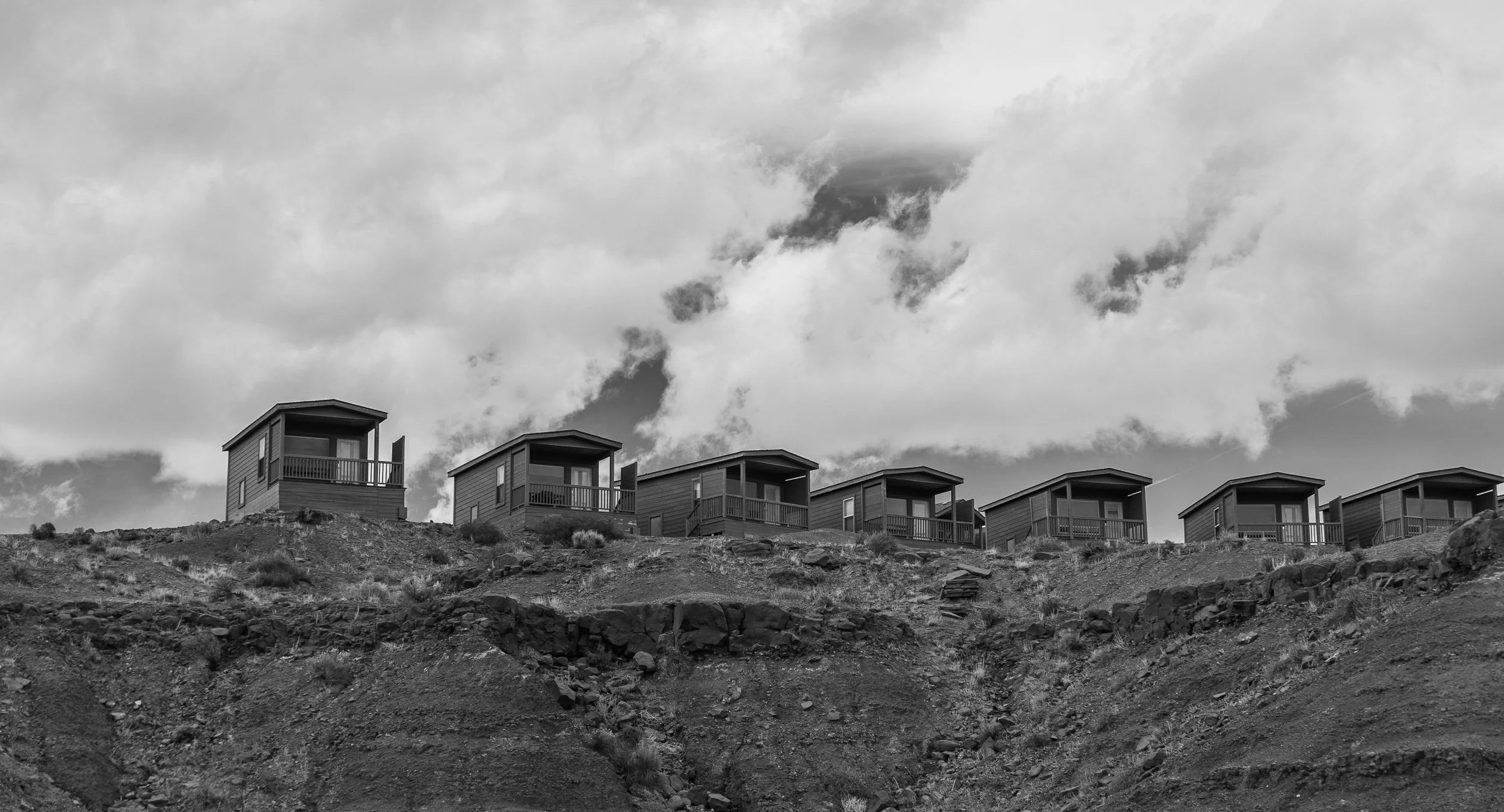 A row of six small houses on a hillside with a cloudy sky overhead.