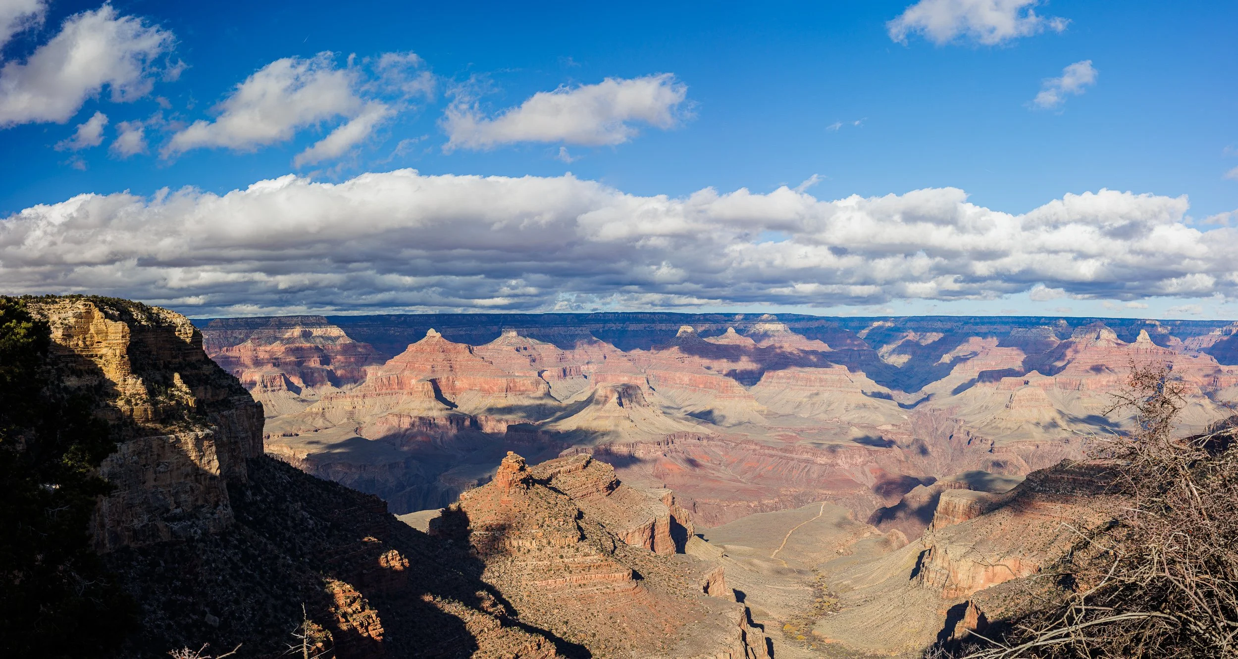 A scenic view of the Grand Canyon with layered rock formations, a partly cloudy sky, and distant horizon.