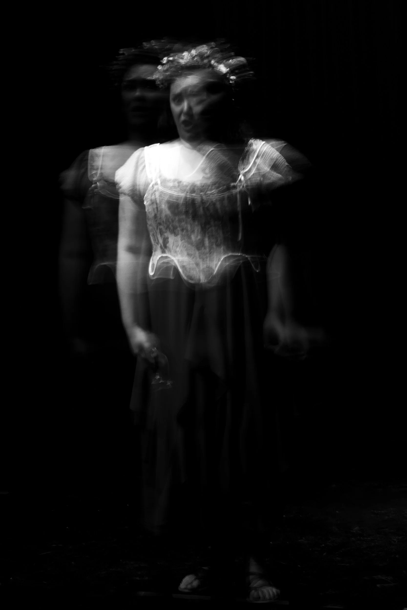 Black and white photo of a woman with multiple exposure effect, appearing to have two faces and body positions, wearing a dress and holding a wine glass, with a dark background.