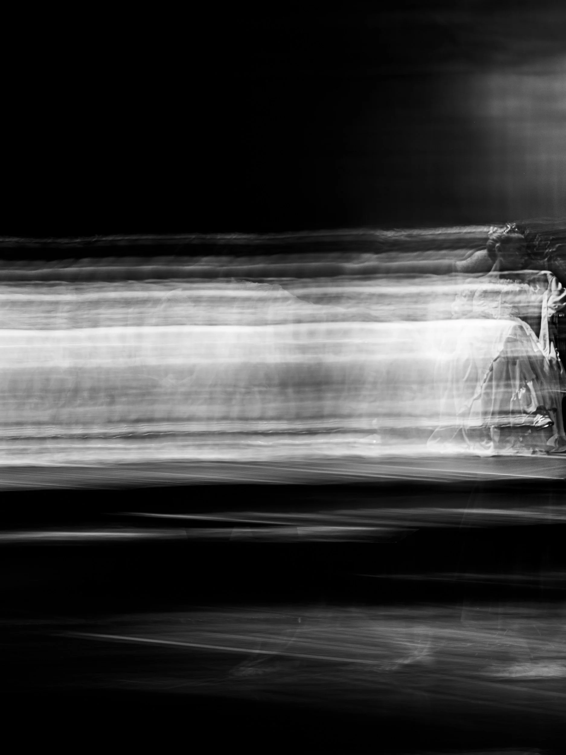Black and white abstract photo with a person sitting on a bench, showing motion blur and long exposure effects