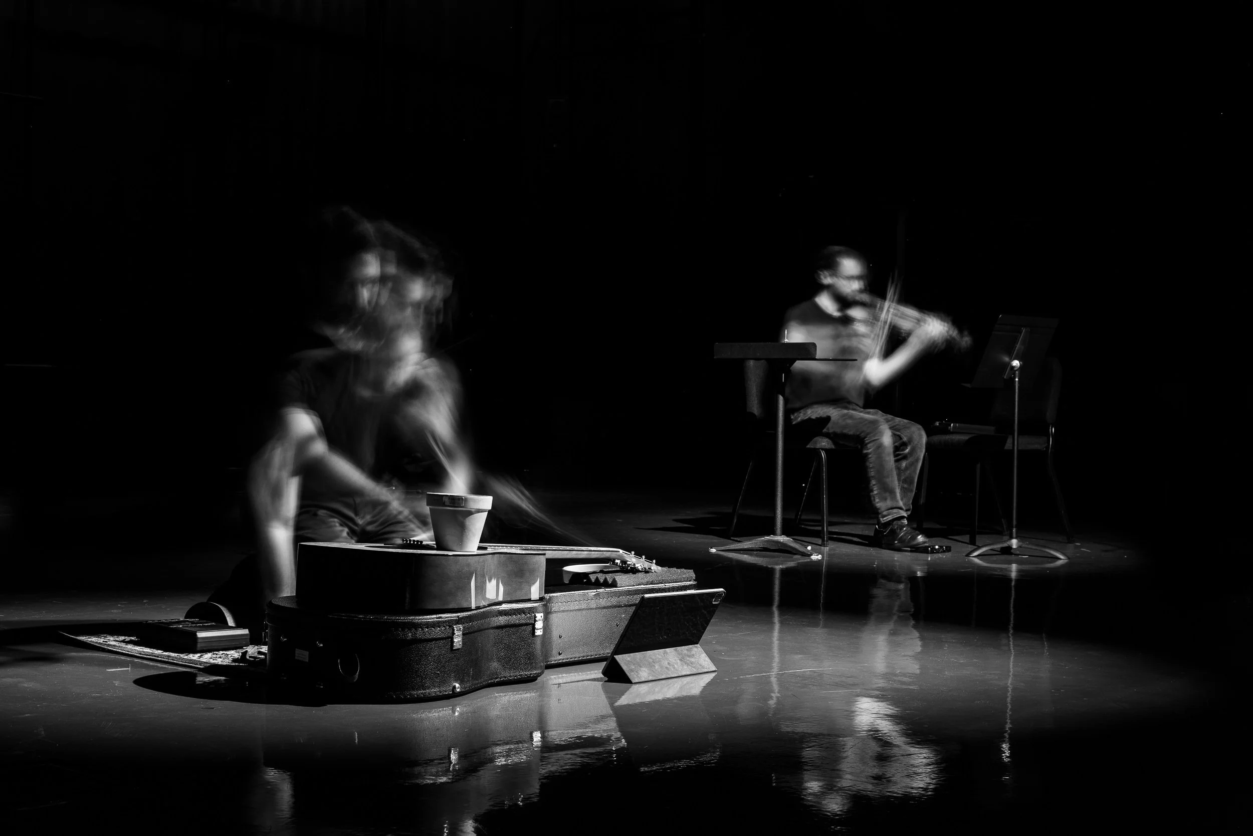 Two musicians performing on a dark stage, one playing a violin and the other an instrument, with a blurry motion effect, creating a dynamic visual.