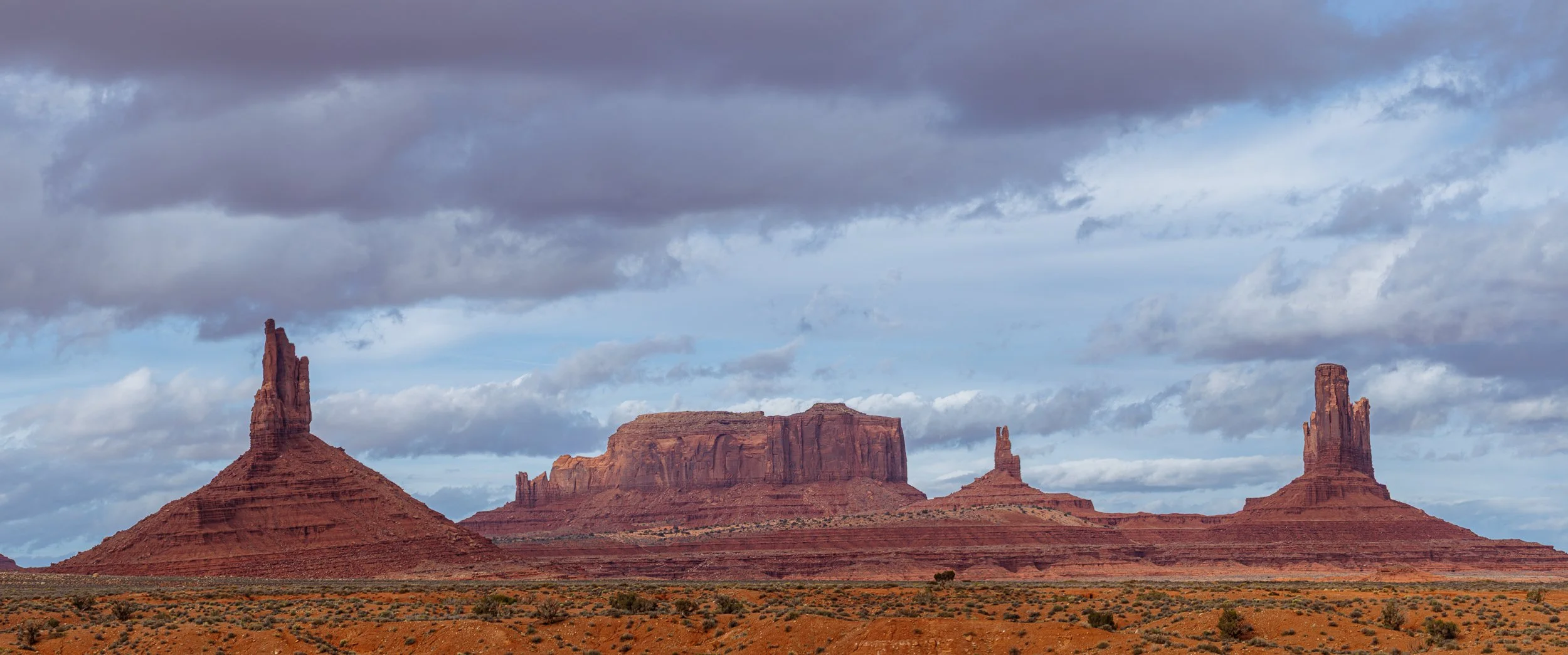 View of Monument Valley with red sandstone mesas and buttes under a cloudy sky.