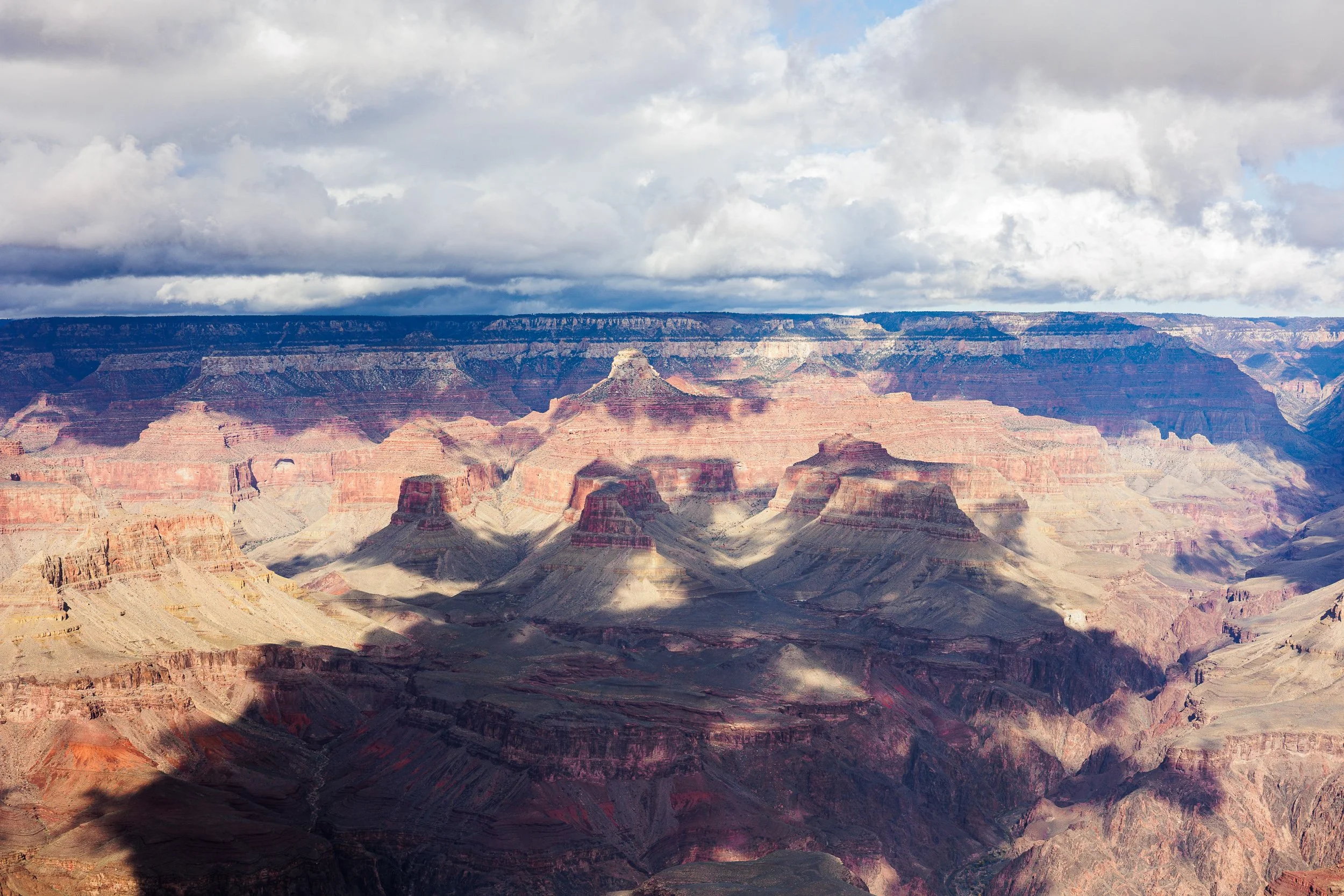 View of the Grand Canyon with layered rock formations and a cloudy sky.