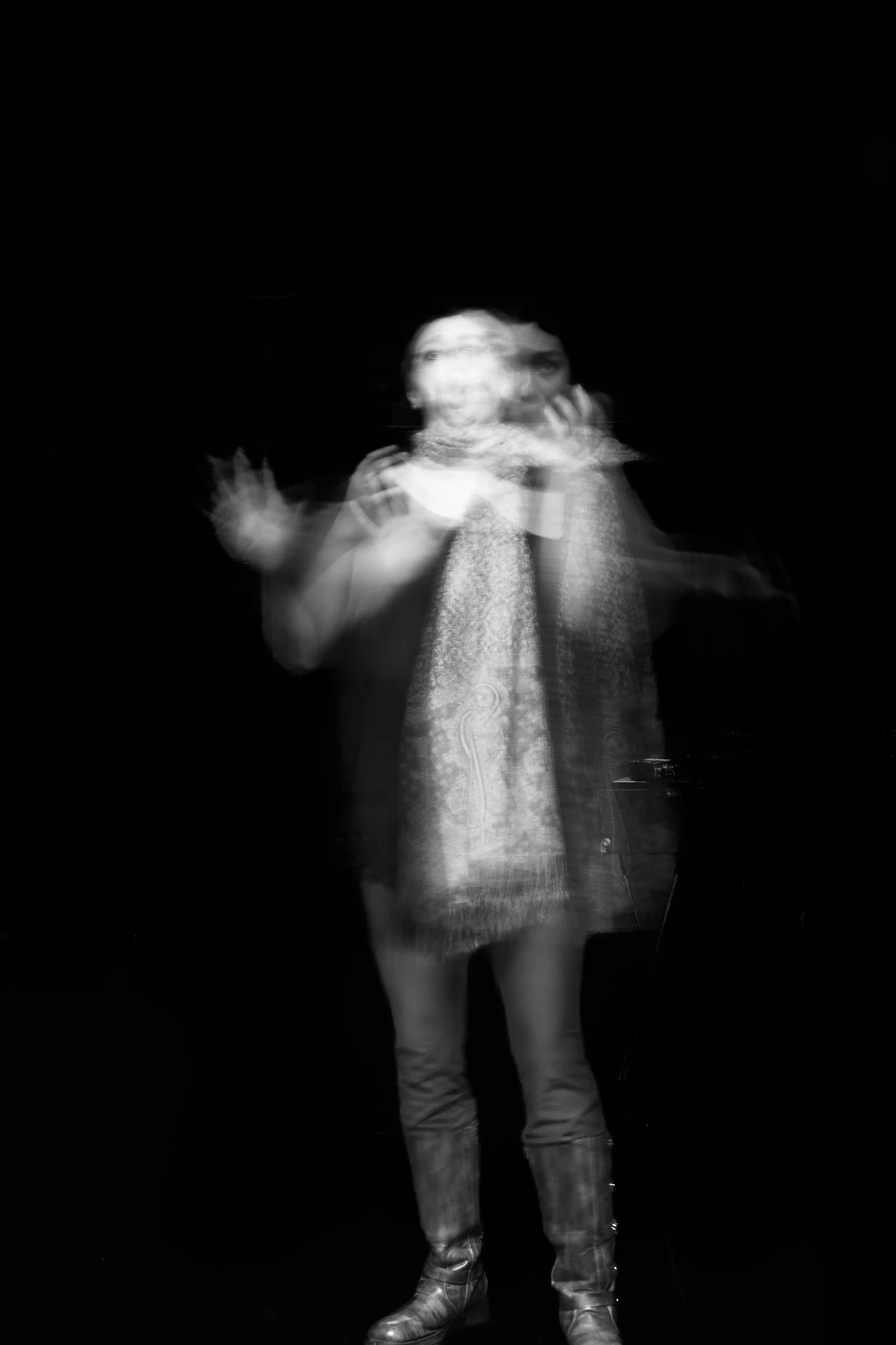 A person standing on stage against a black background, with motion blur and ghosting effects, making the person's figure appear layered and blurry.