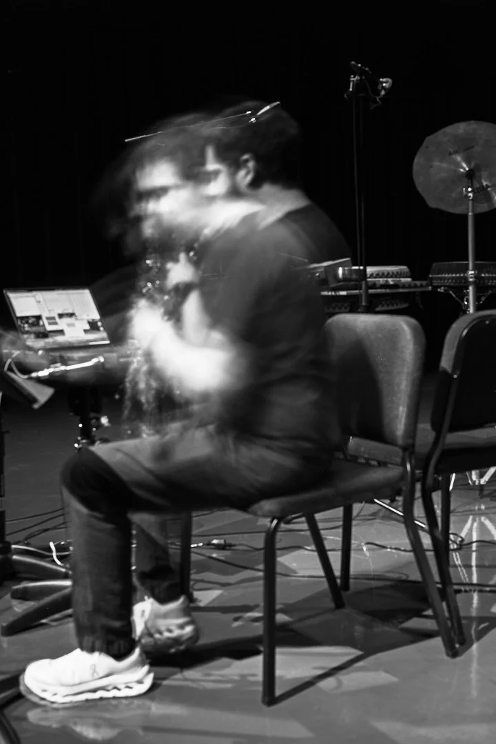 A person sitting on a chair, moving rapidly in front of a camera, creating a blurred motion effect in black and white.