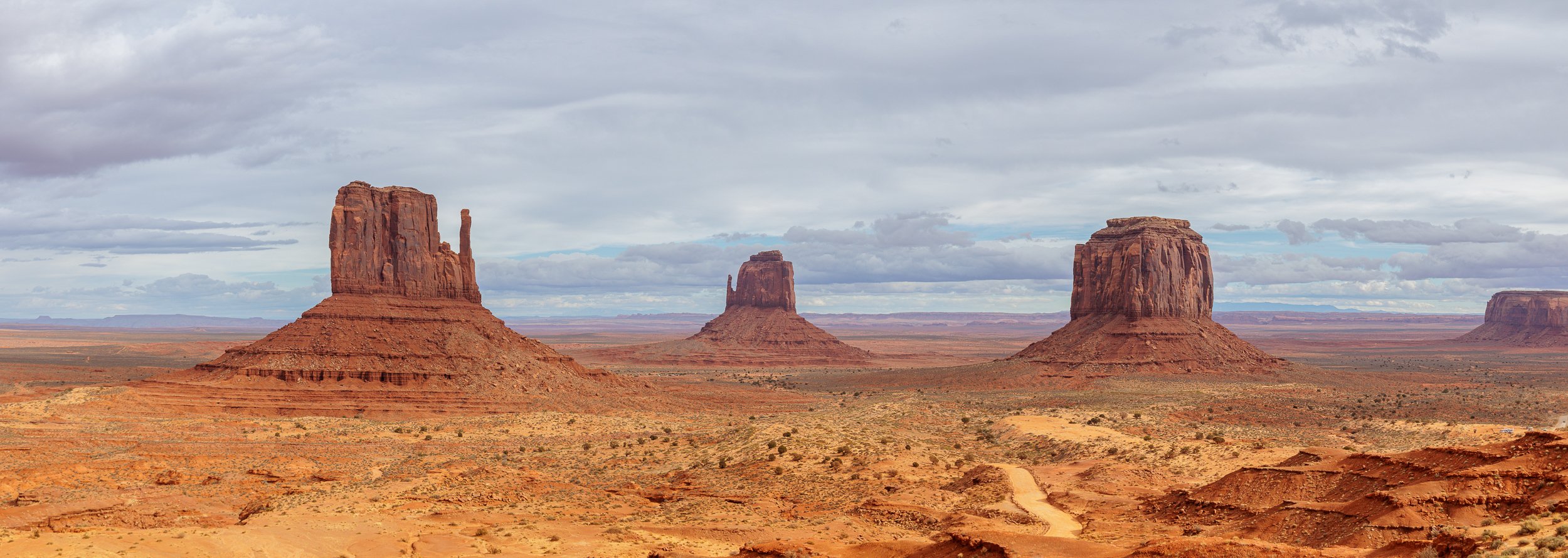 Three large rock formations in a desert landscape with a cloudy sky overhead.