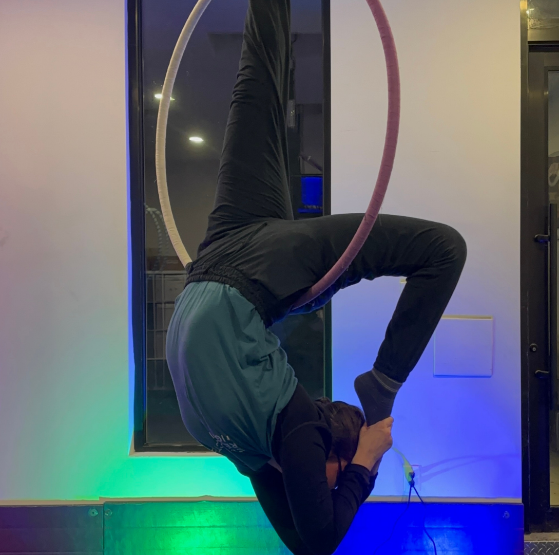 Person performing aerial hoop acrobatics in a modern indoor setting with colorful lighting.