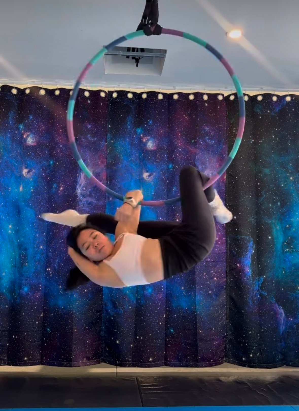 A woman performing a hoop dance inside a room with galaxy-themed curtains in the background.