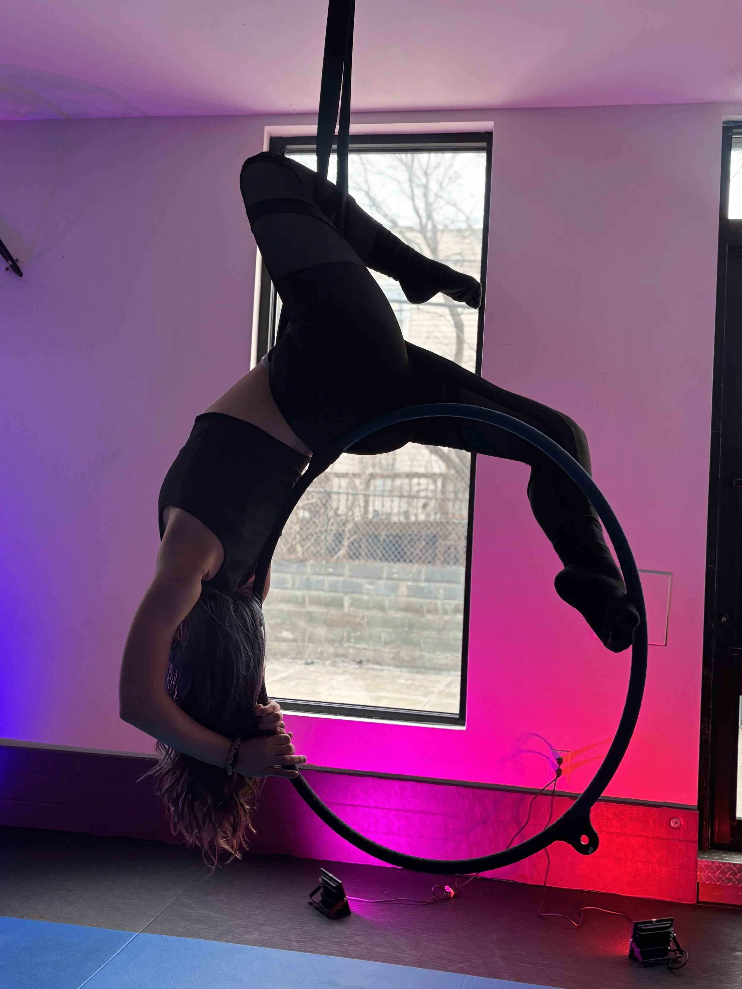 A woman hanging upside down from purple aerial silk in front of a galaxy-themed curtain.