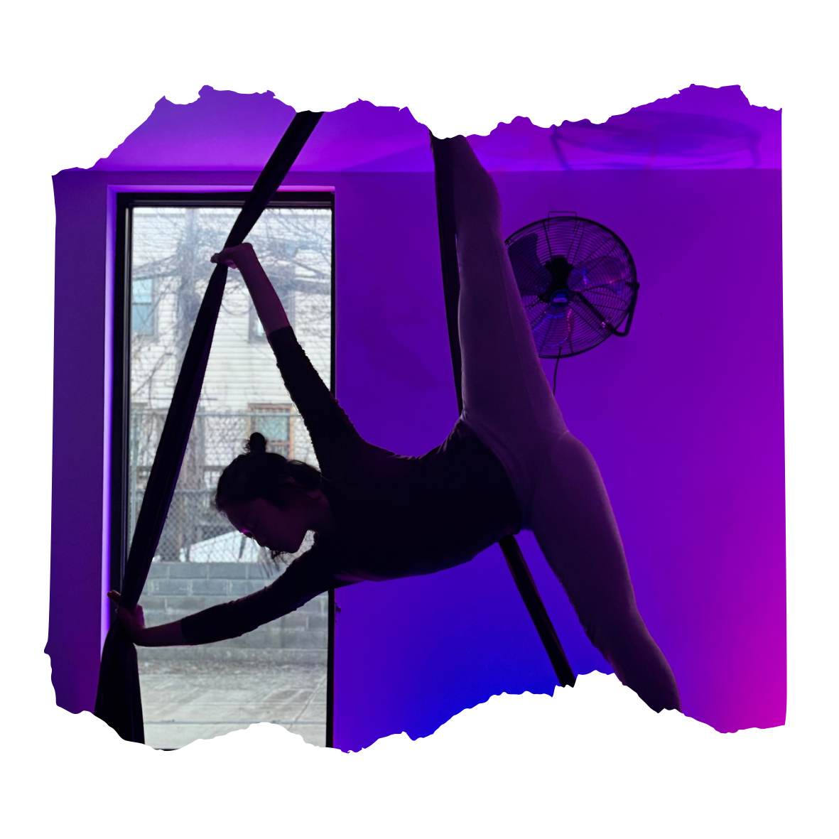 Silhouette of a woman practicing aerial yoga on fabric next to a window with purple lighting.