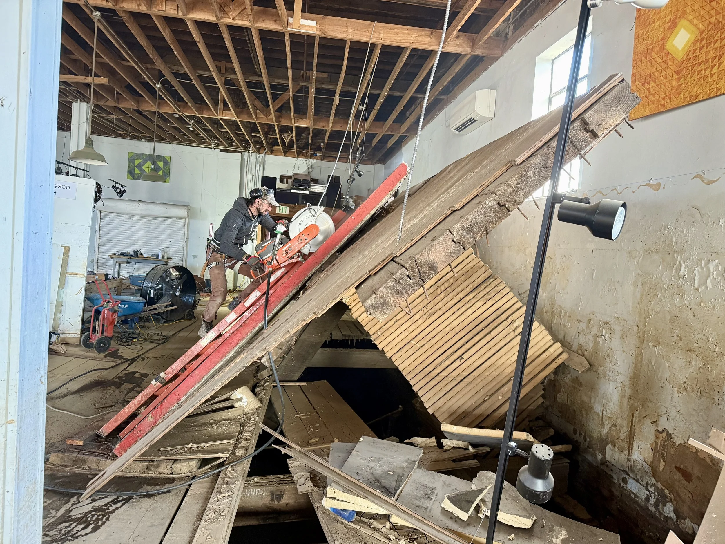 A worker using a saw to cut through a collapsed wooden ceiling after structural damage.