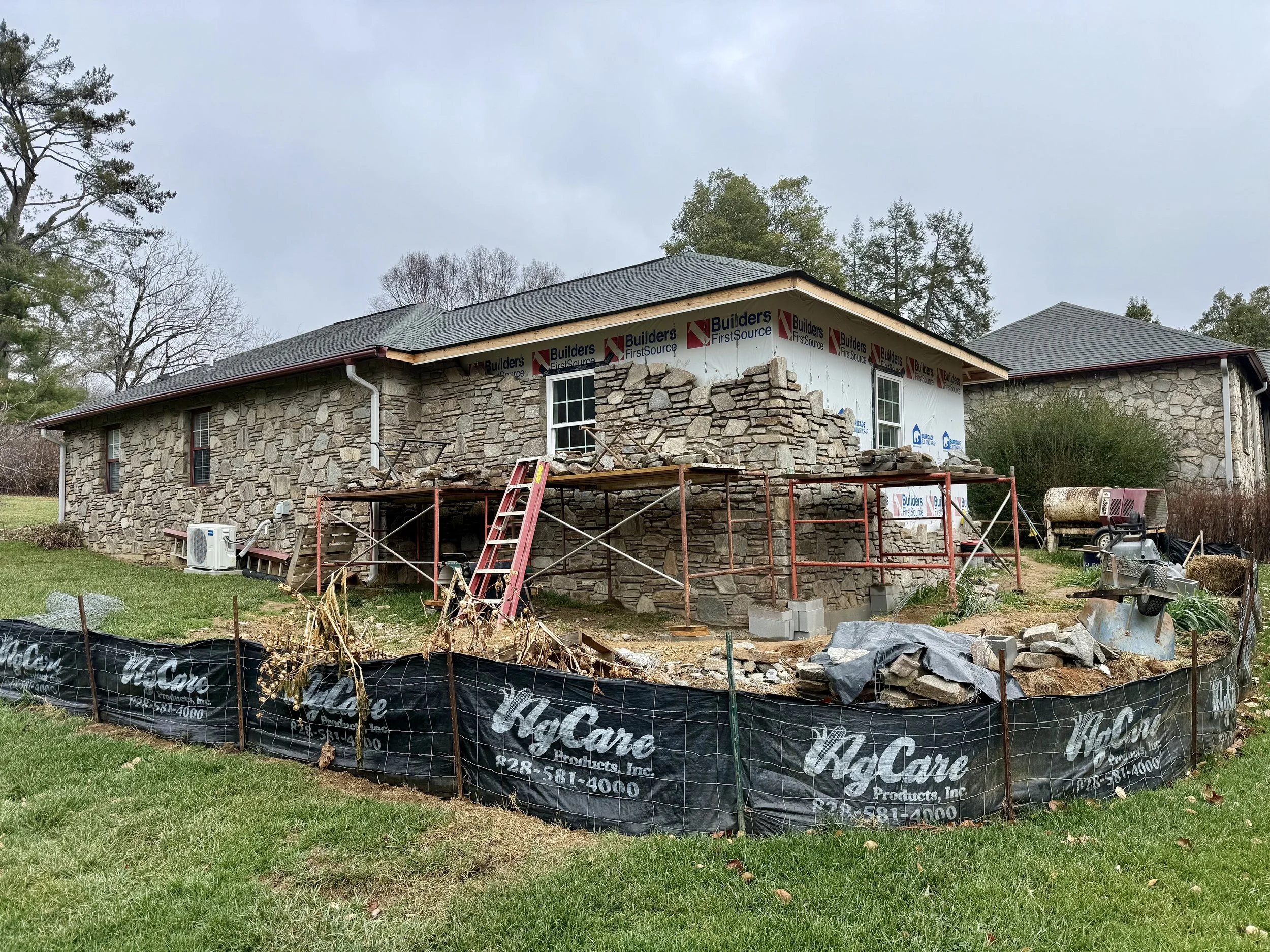 A house under construction with stone walls and a partially installed roof, surrounded by building materials and equipment, indicating ongoing renovation work.