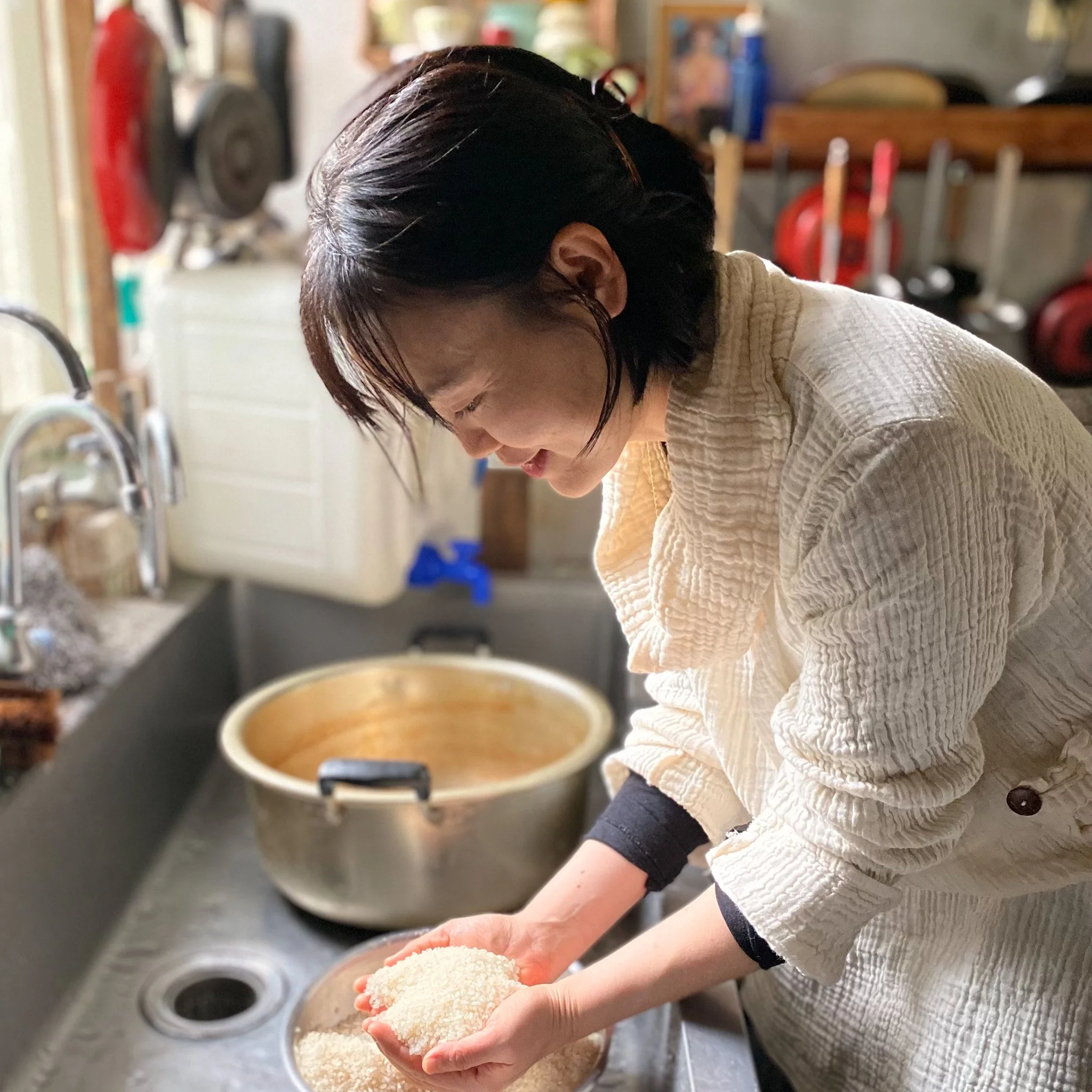 A woman with short dark hair washing rice in a kitchen sink.