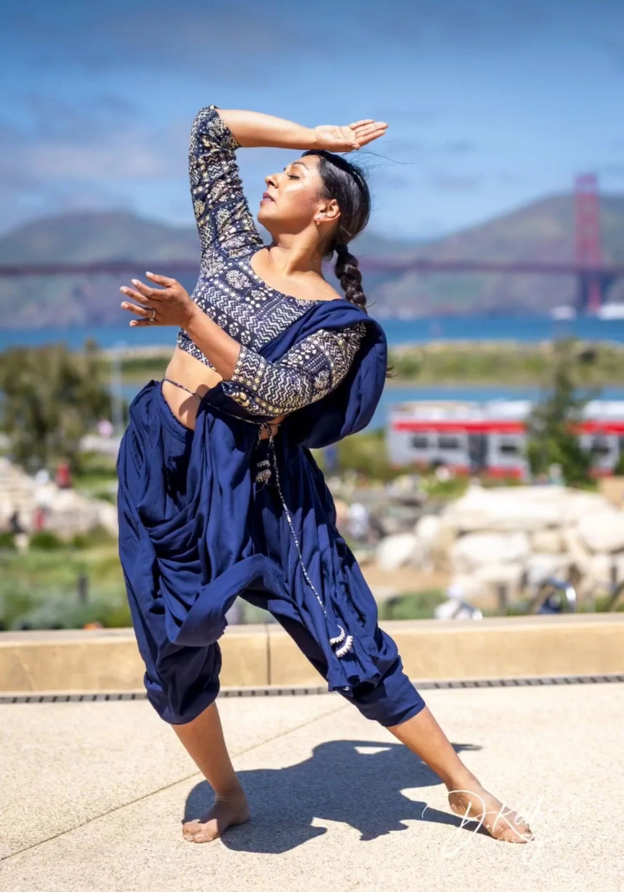 Woman performing a traditional Indian dance outdoors with the Golden Gate Bridge in the background