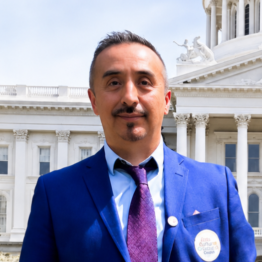 Man in a blue suit and purple tie standing in front of the U.S. Capitol building