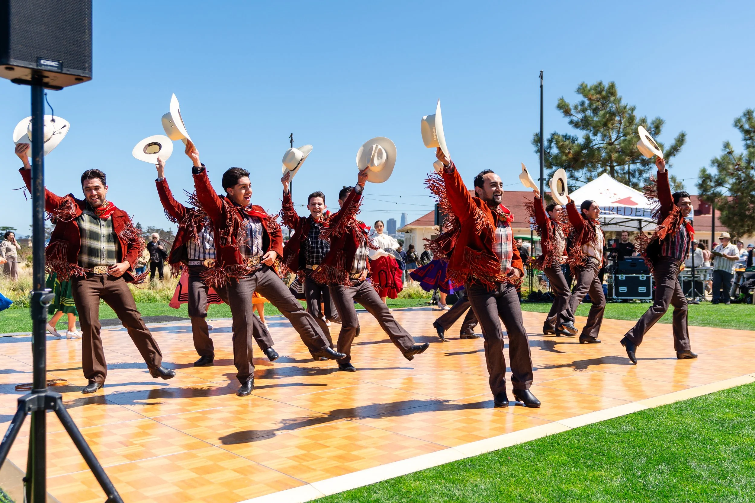 Performers in red fringed jackets and cowboy hats dancing on an outdoor stage.