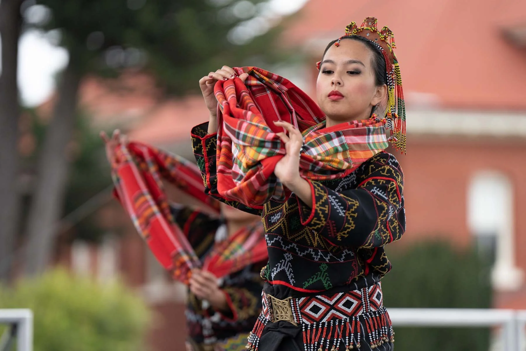 Woman in traditional embroidered clothing and ornate headdress performing with a red patterned textile
