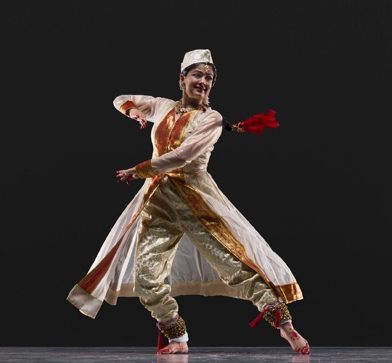 Indian classical dancer performing in ornate white and gold traditional costume against a black background