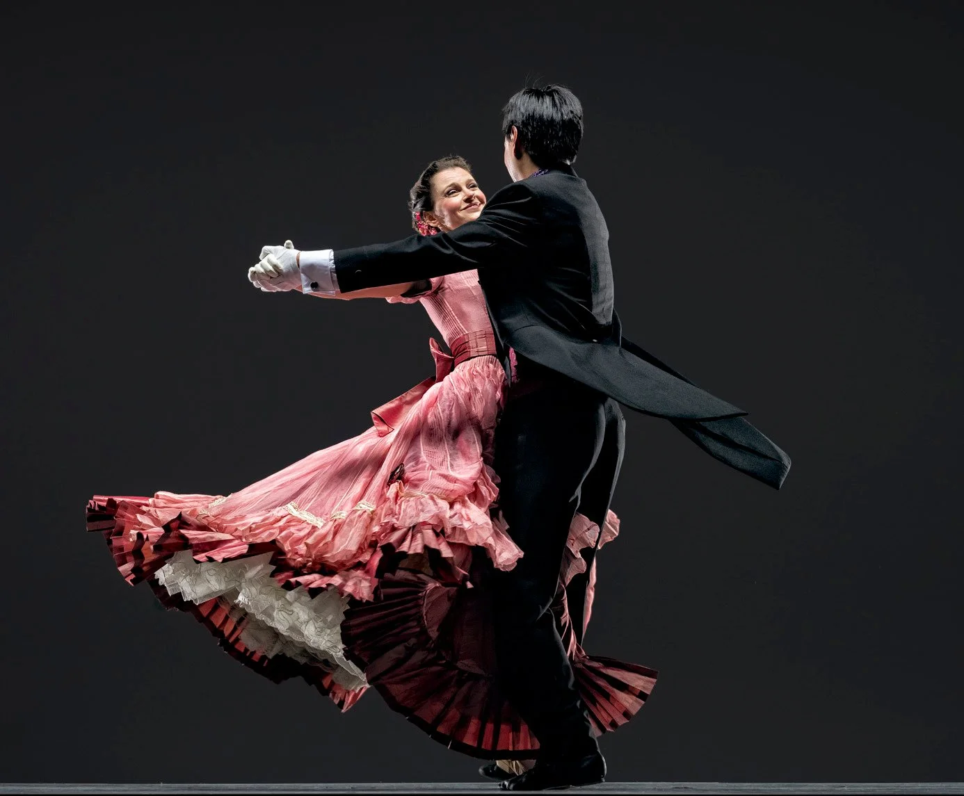 Ballroom dancers performing a dramatic turn, with the woman in a flowing pink dress and the man in a black tailcoat.