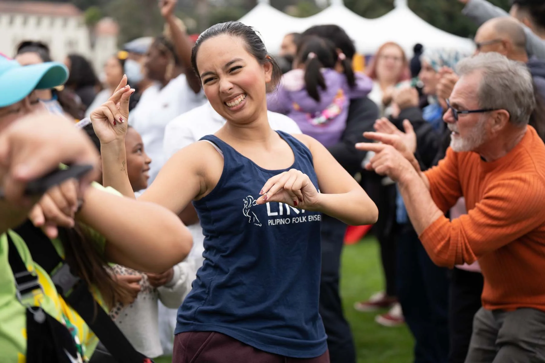 Smiling woman dancing with a crowd at an outdoor Filipino folk dance event