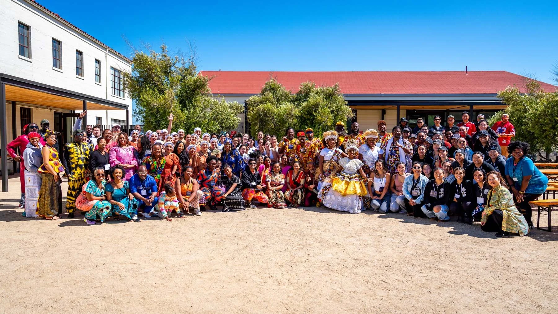 Large diverse group in colorful cultural clothing posing outside a school courtyard