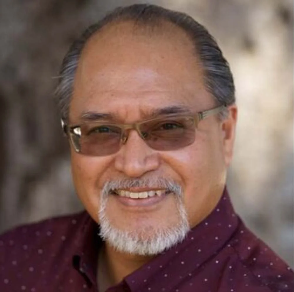 Portrait of a smiling older man with glasses and a white goatee wearing a burgundy shirt