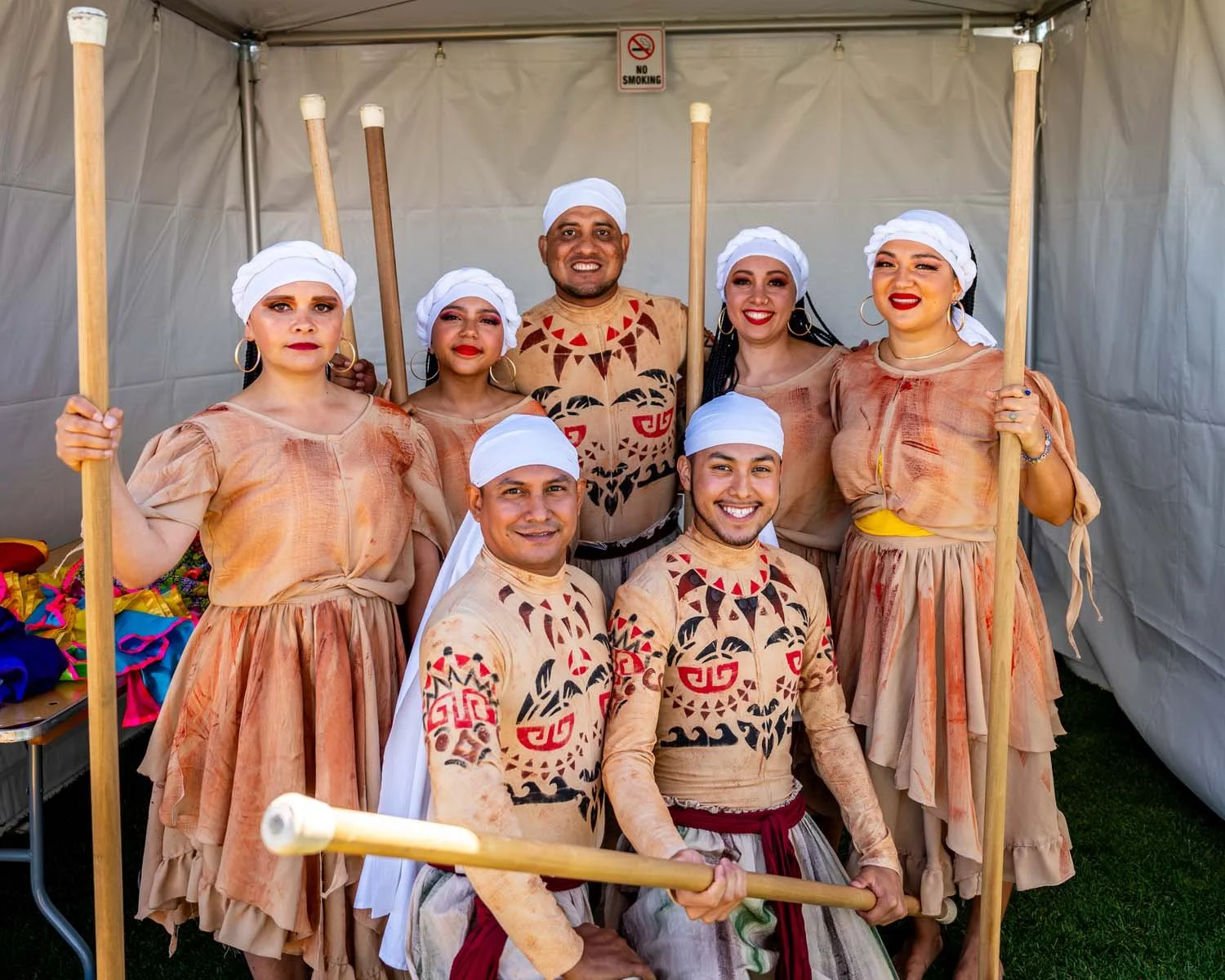 Group of costumed performers posing with wooden staffs inside a tent