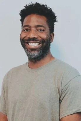 Smiling bearded Black man wearing a gray T-shirt against a light gray background