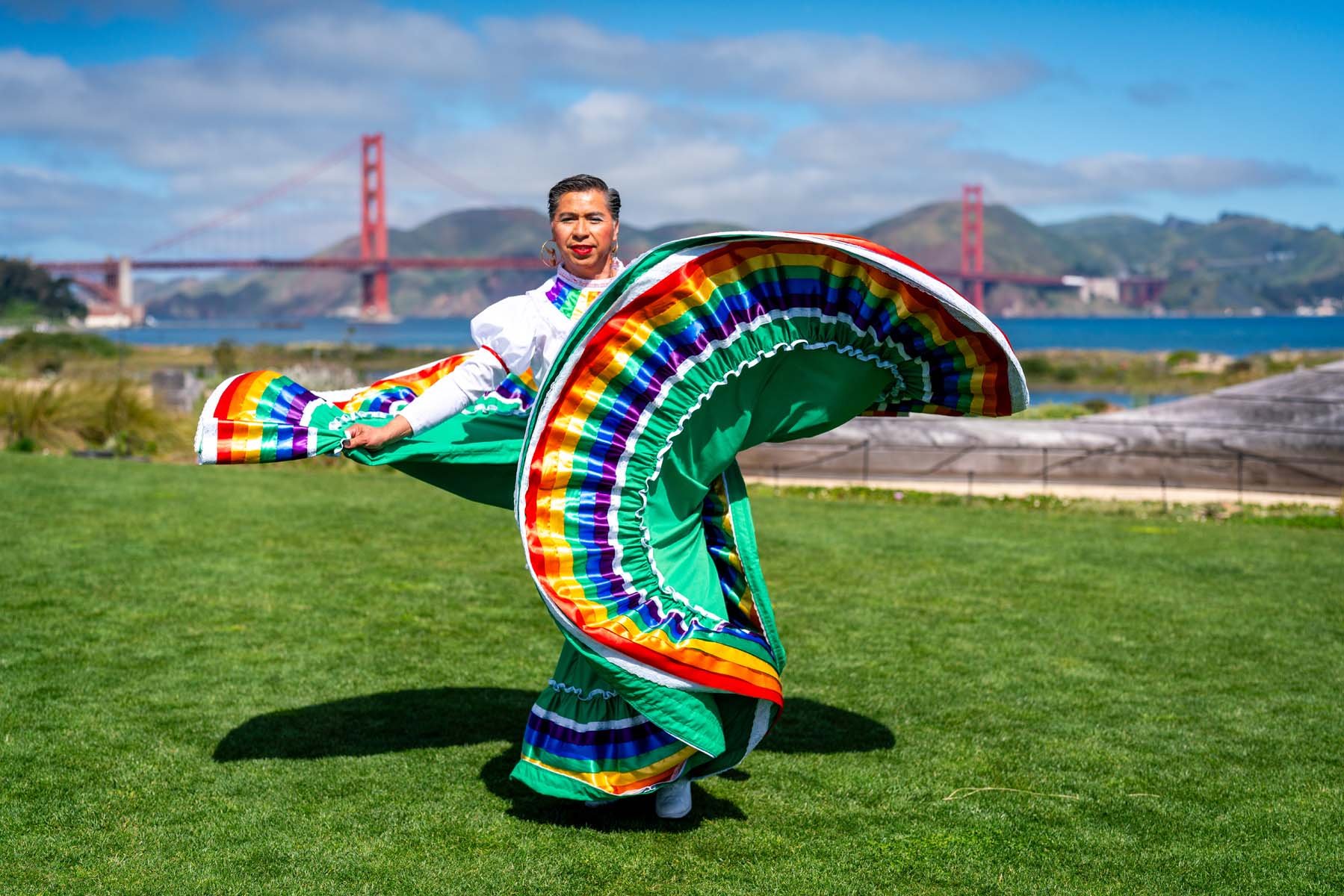 Dancer in a colorful traditional Mexican dress performs on a lawn with San Francisco’s Golden Gate Bridge in the background.