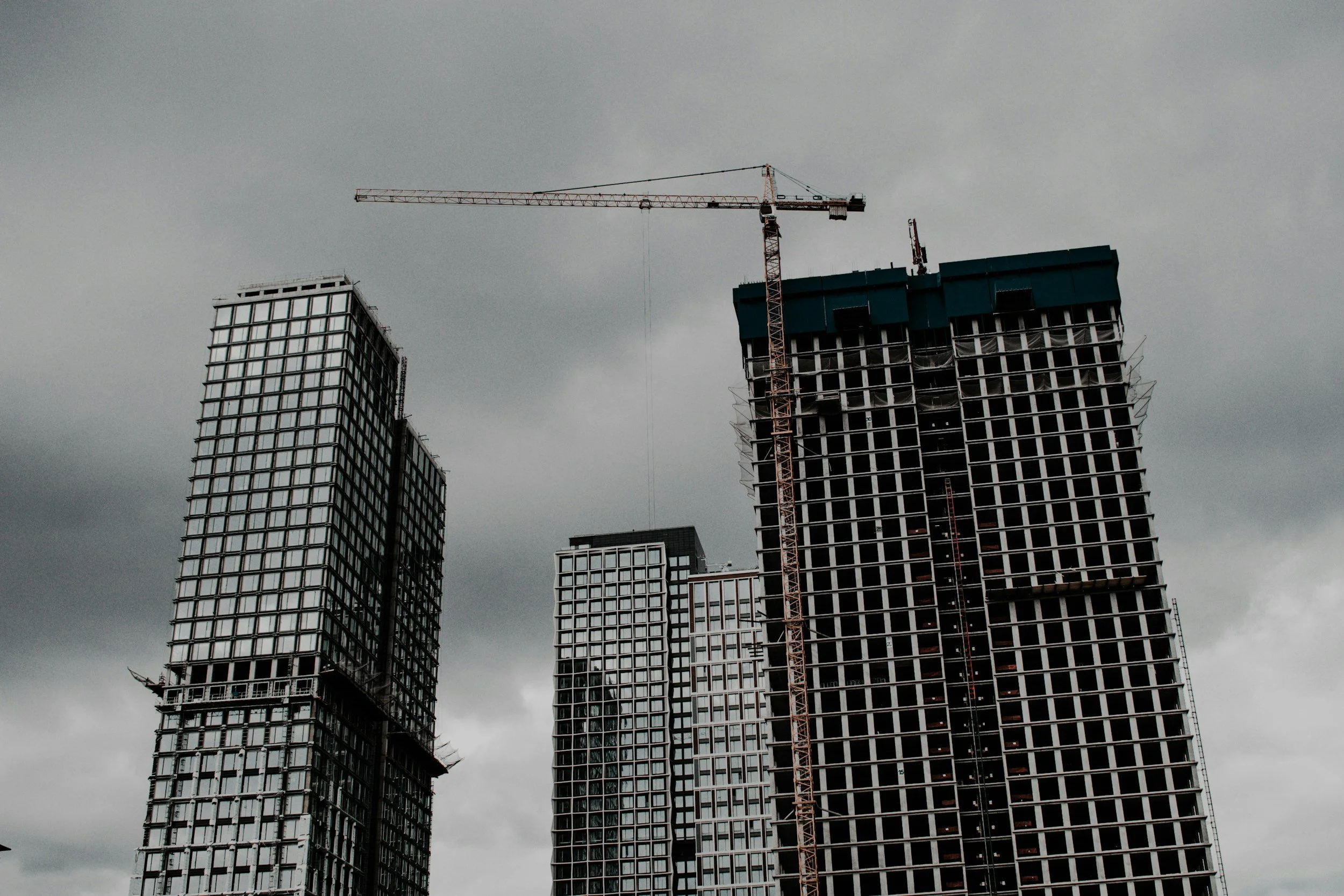 Under construction high-rise buildings with a crane against cloudy sky.