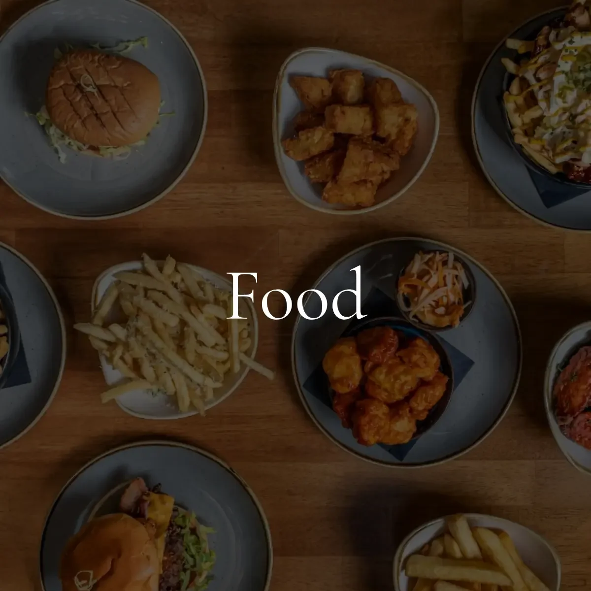 Assorted dishes of American fast food including a burger, fries, fried chicken pieces, a salad, and other side dishes on a wooden table.