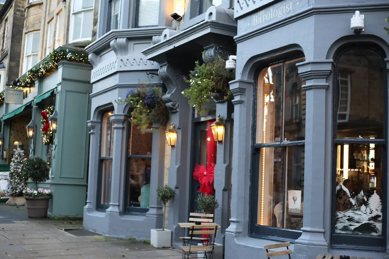 Decorated storefront with holiday decorations, including Christmas wreaths and garlands, potted plants, and outdoor seating.